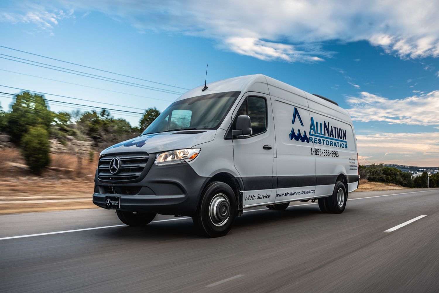 A Mercedes-Benz delivery van drives on a highway under blue skies.