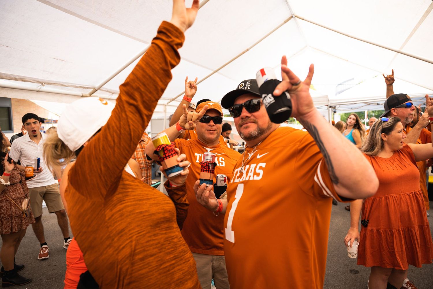 Fans in orange jerseys celebrate enthusiastically under a white event tent.
