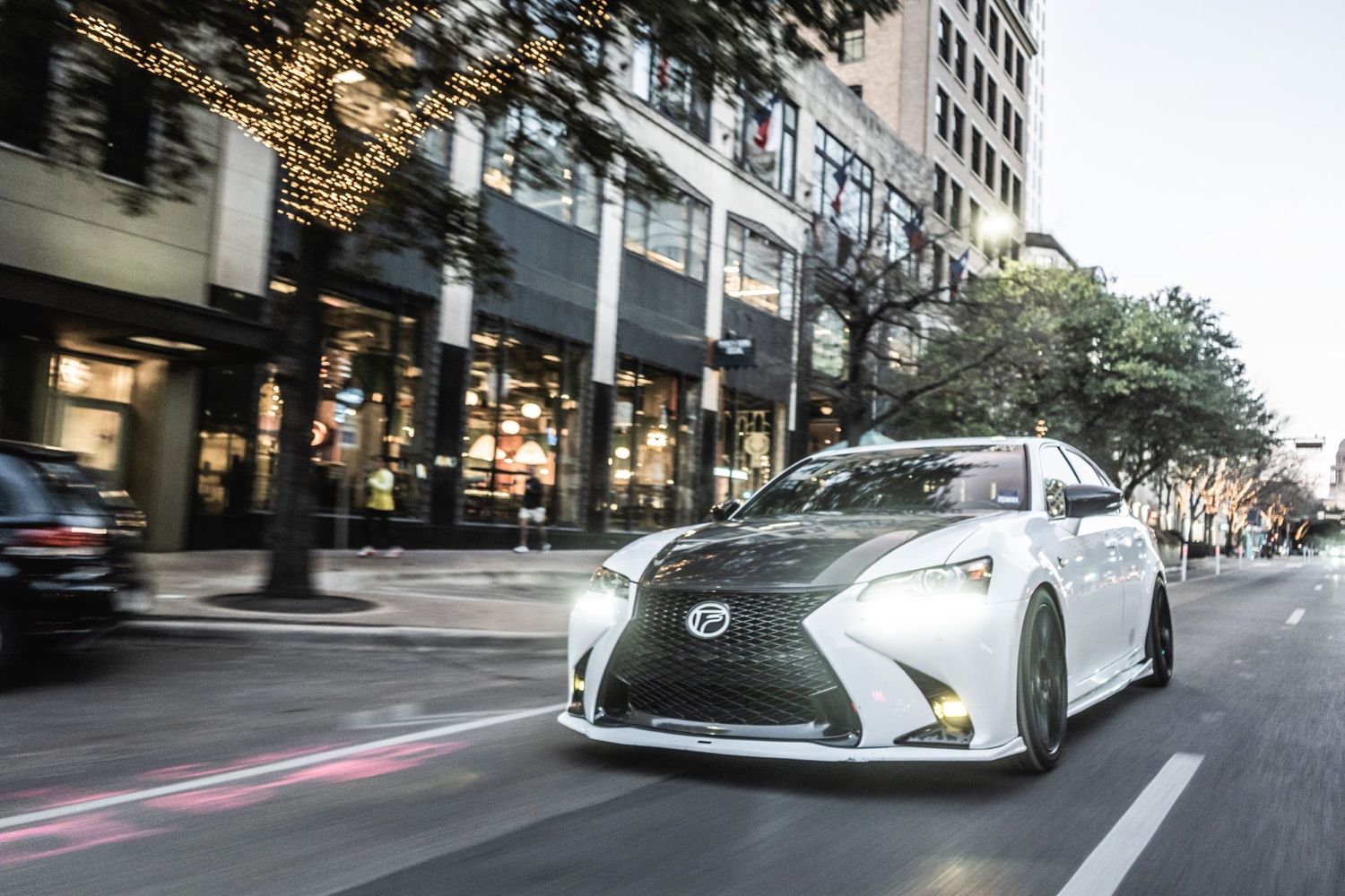 White Lexus sports car driving through downtown city streets with motion blur effect.