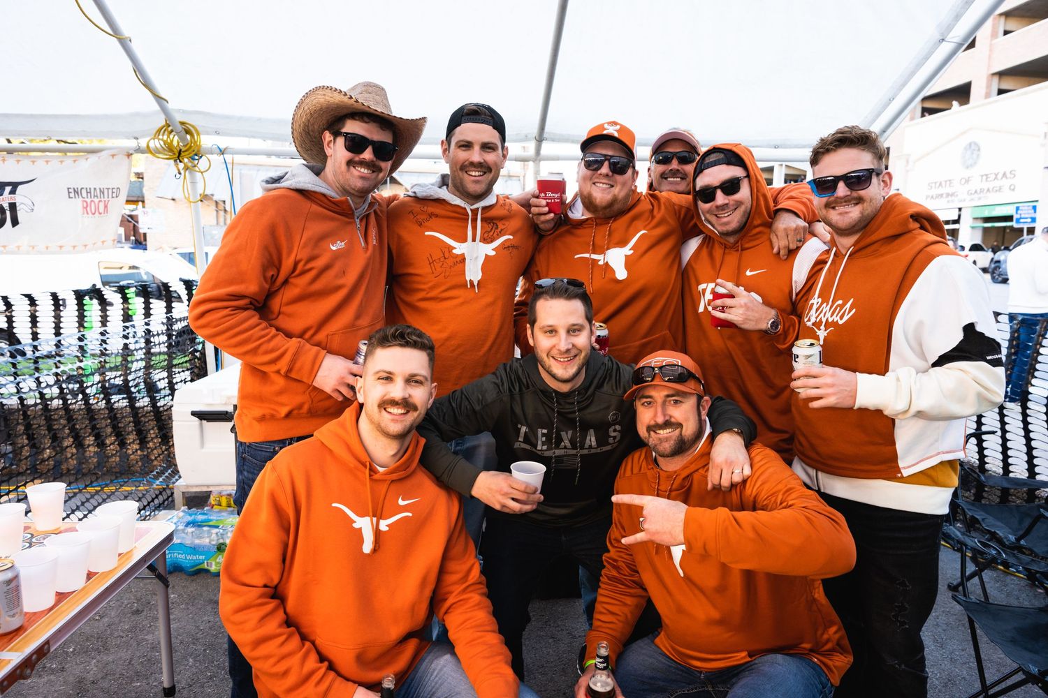 Group photo of sports fans wearing matching orange team hoodies at a tailgate party.