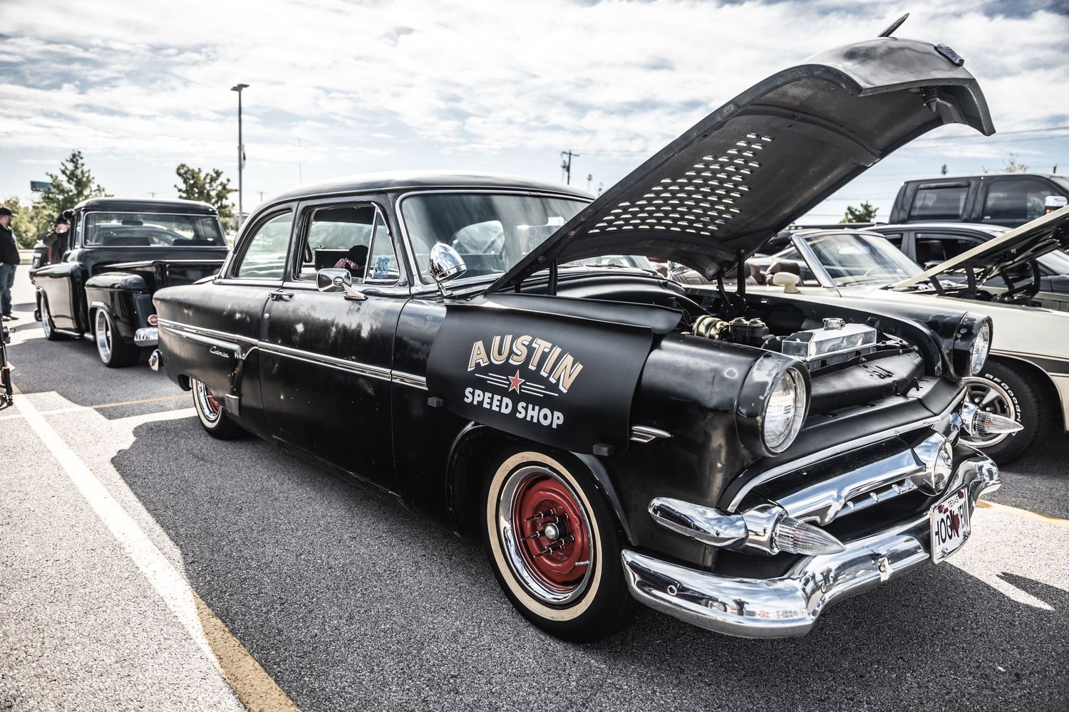 Black vintage Ford with open hood displaying custom engine at car show.