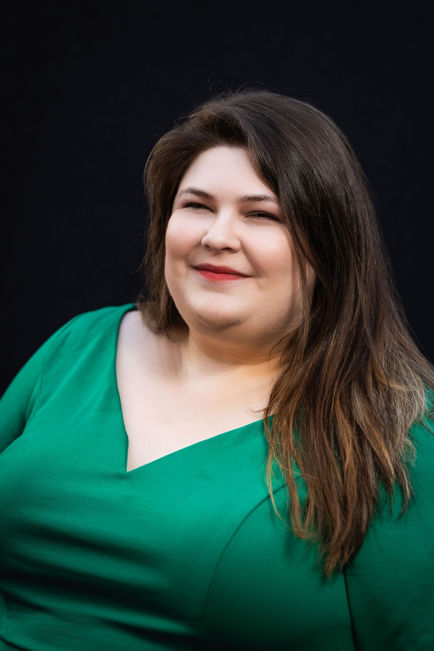 Professional headshot of woman in green dress smiling against black background.