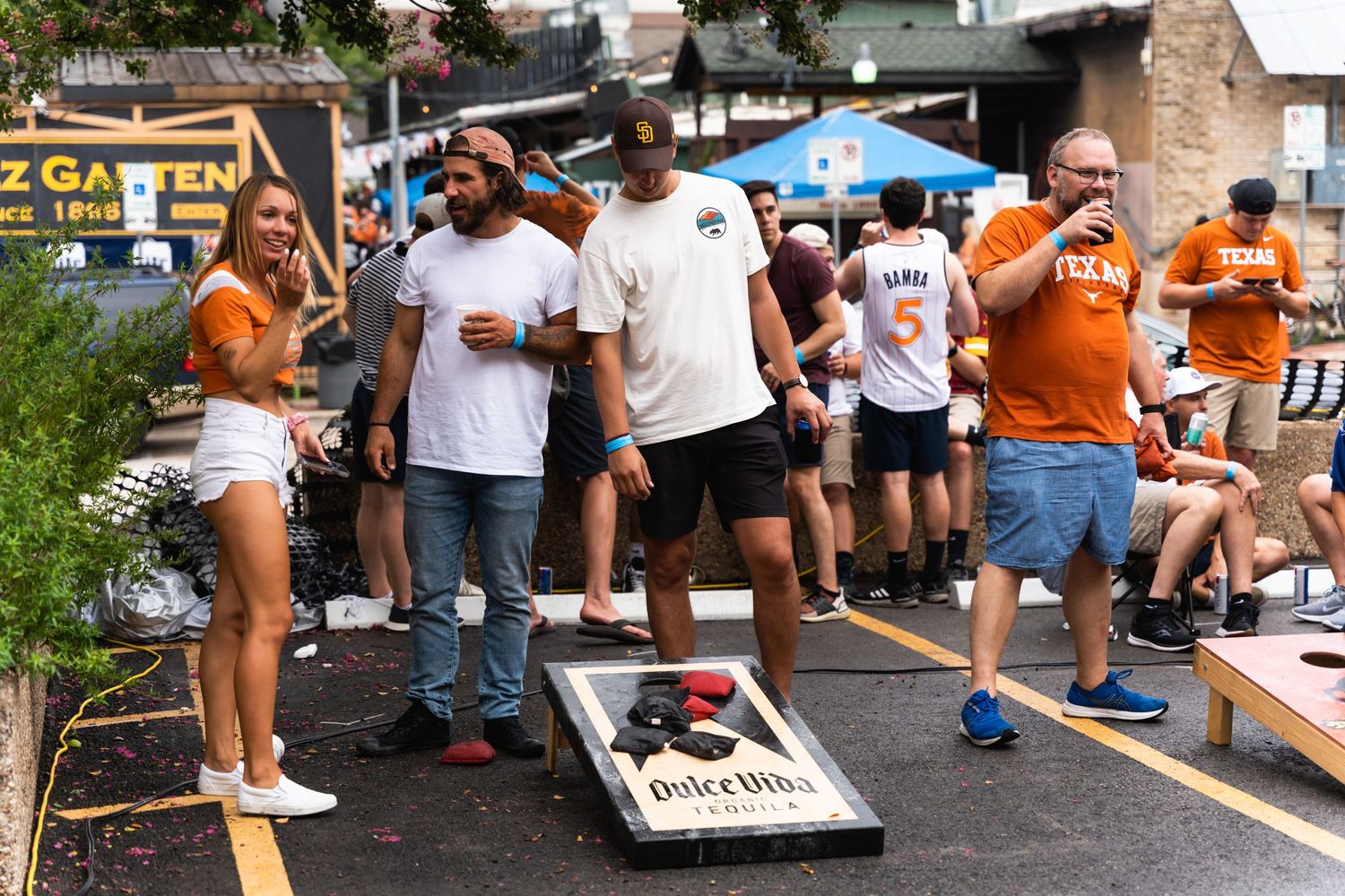 Group plays cornhole game at outdoor tailgate party.