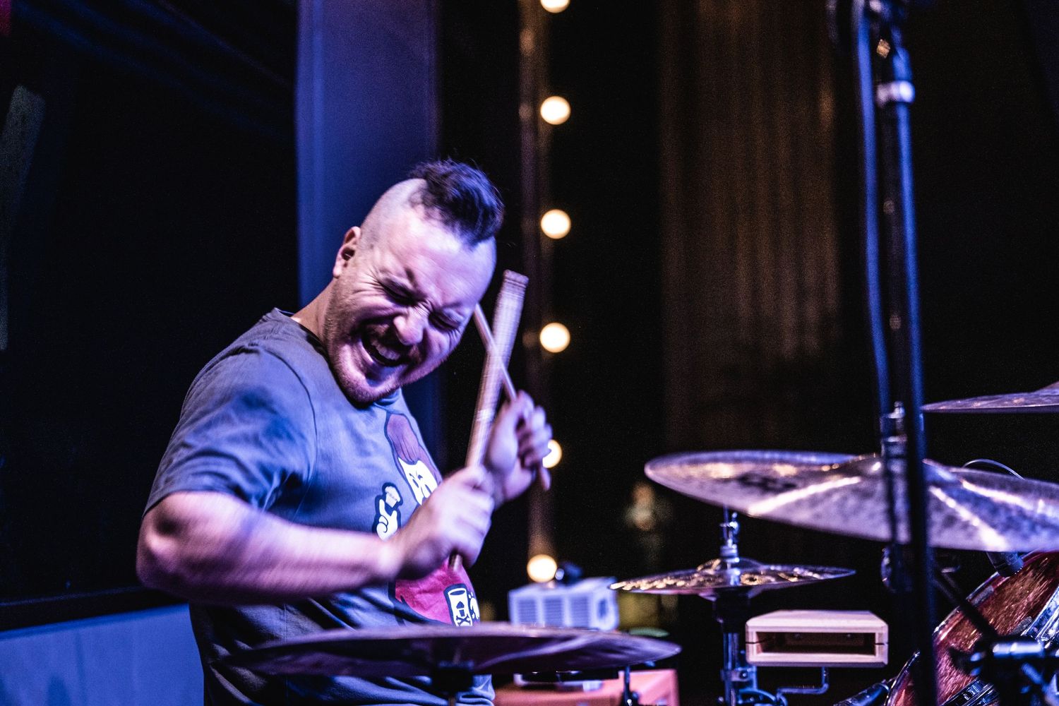 Energetic drummer performs on stage with dramatic concert lighting.