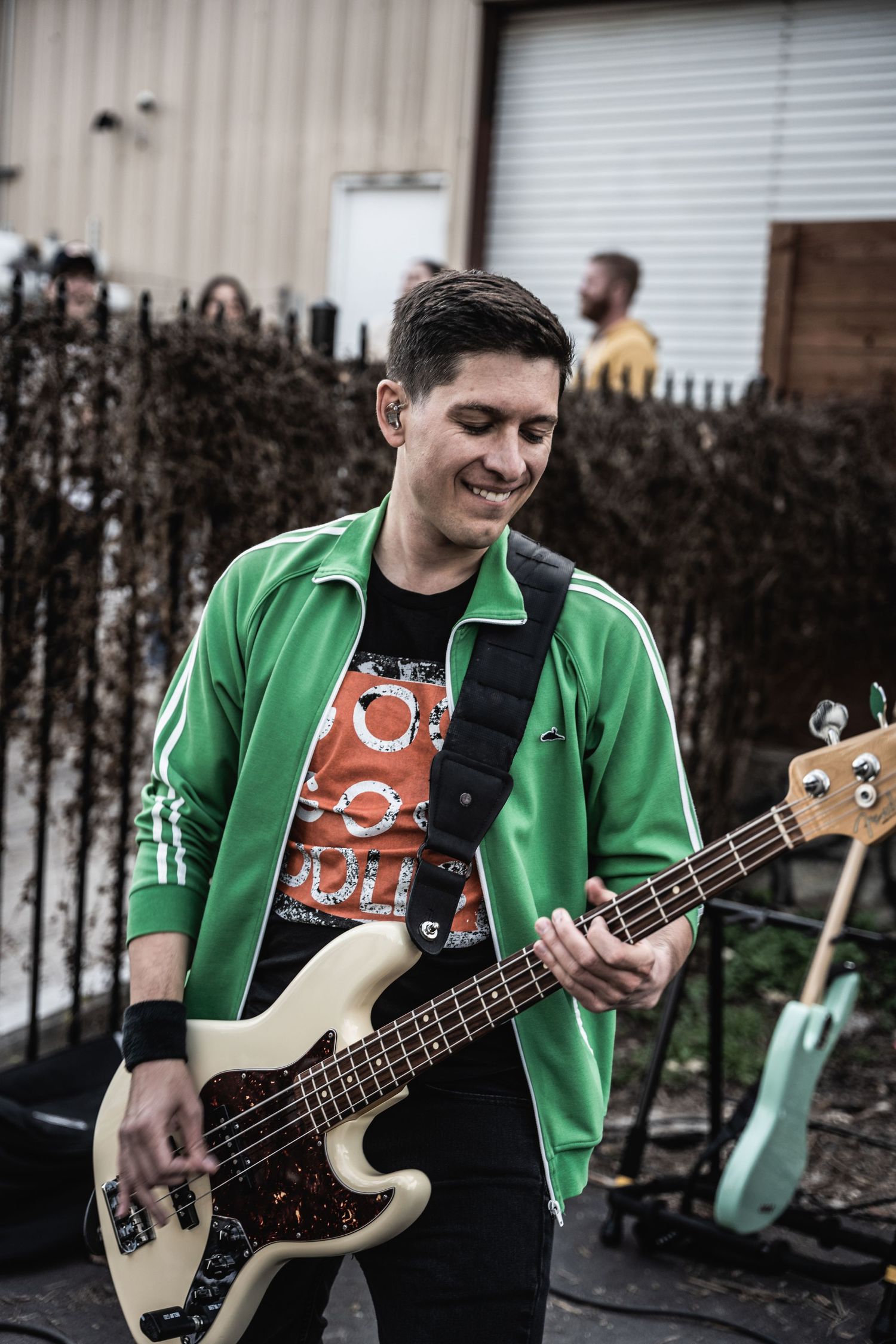 Bass player in green jacket smiling while performing outdoors.