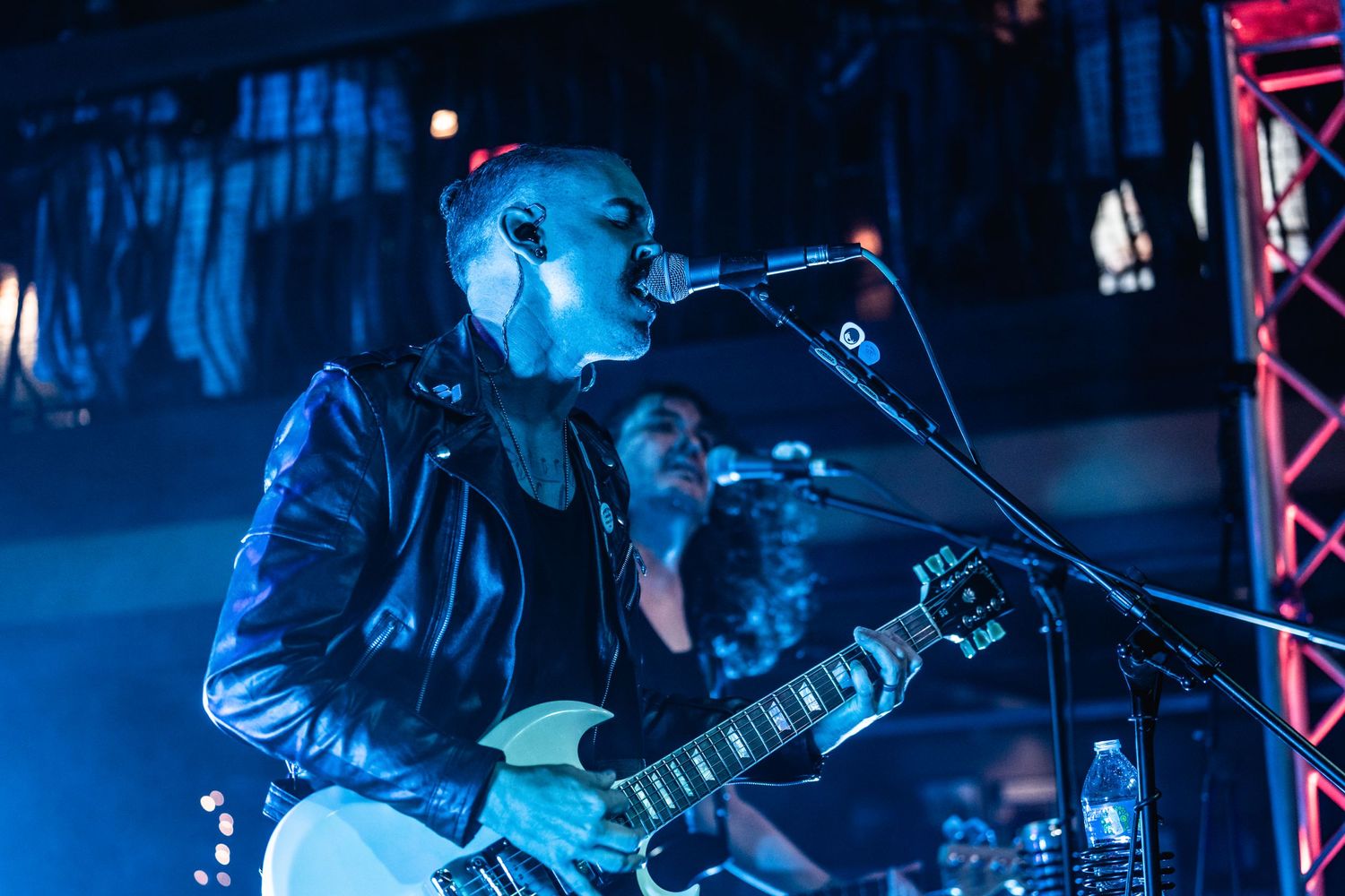 Concert performer singing into microphone under dramatic blue stage lighting.