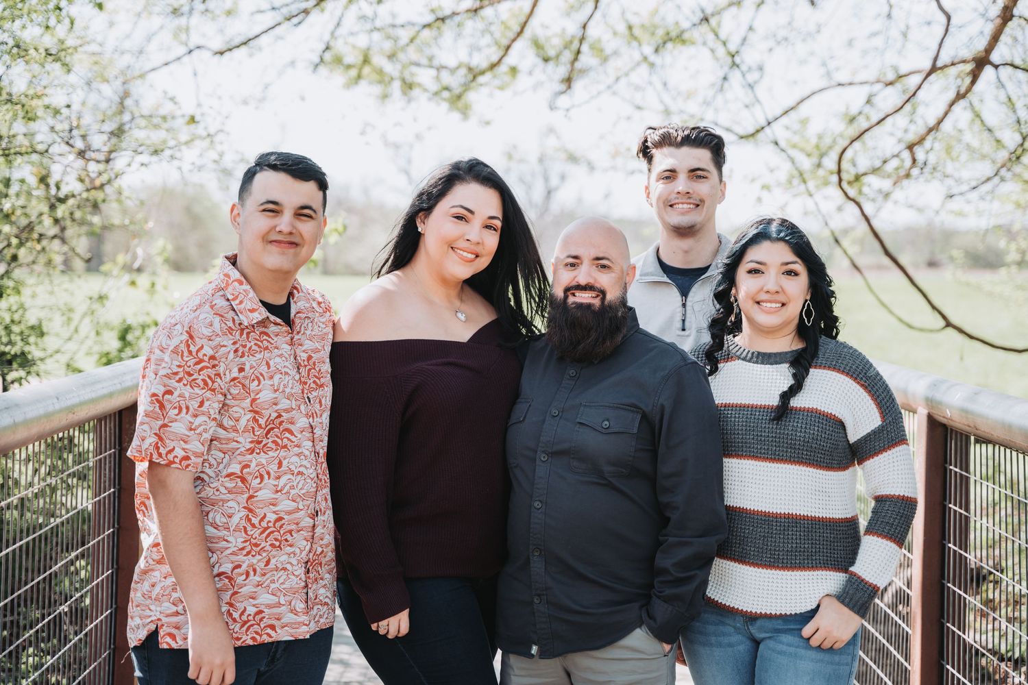 Group of friends gather on a wooden bridge for a casual outdoor photo during springtime.