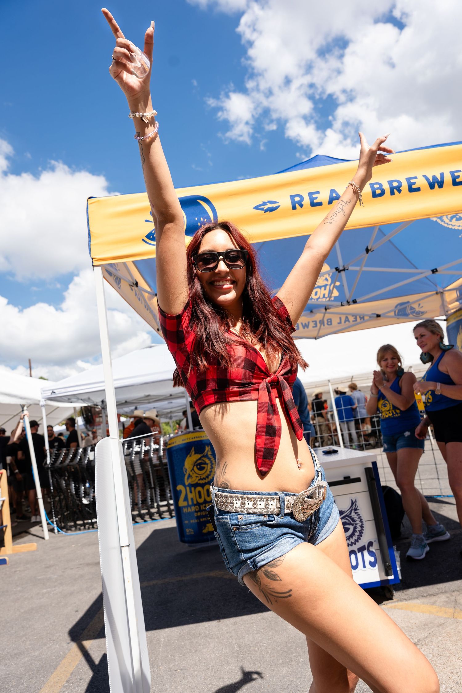Woman in plaid crop top and denim shorts celebrates at Real Brews festival.