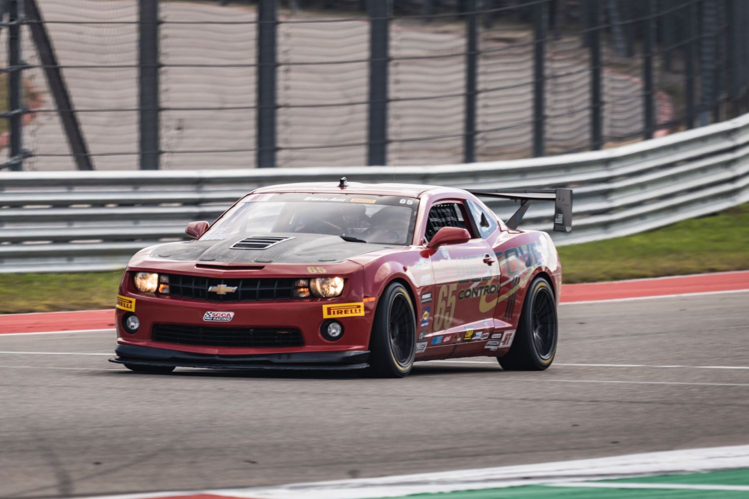 Red Chevrolet Camaro race car navigates through a racing track curve.