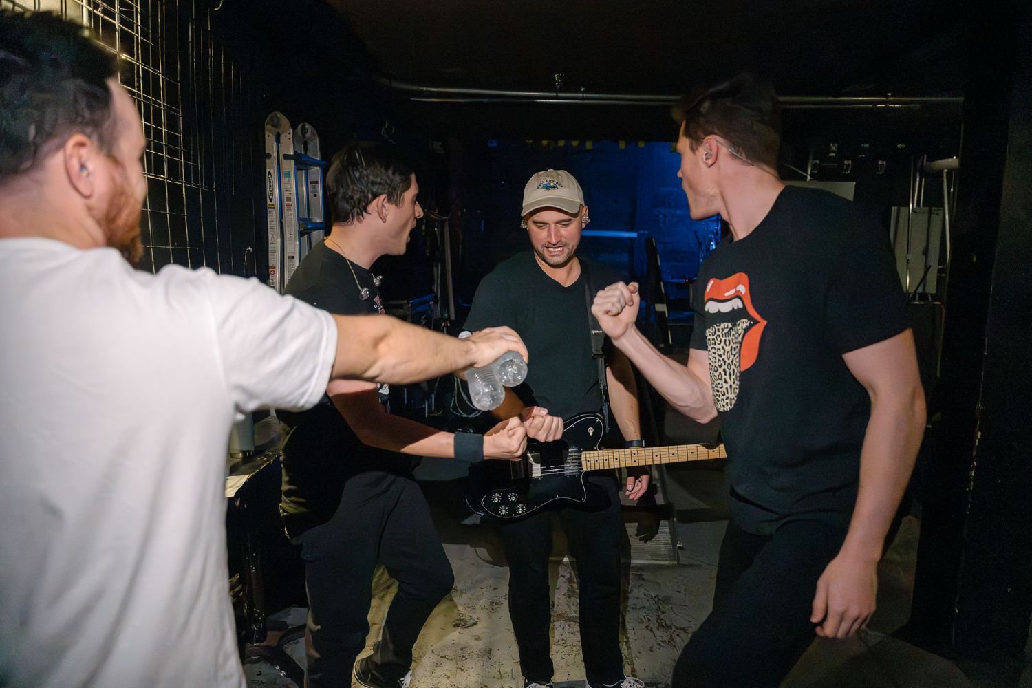 People interact in a dimly lit backstage area during what appears to be a band event.