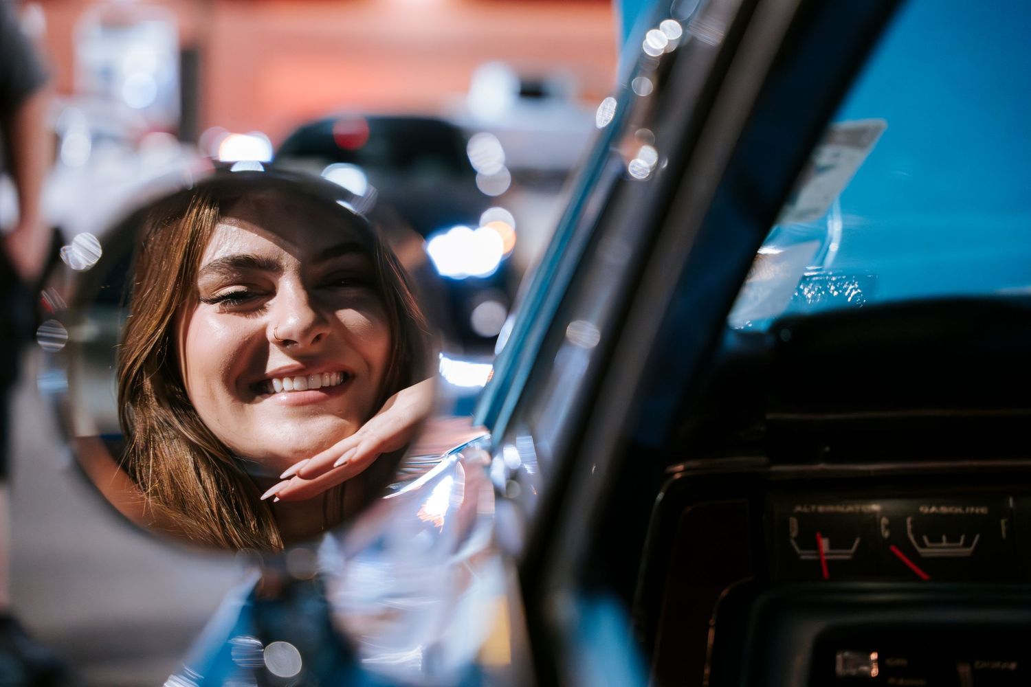 Smiling person peers through car window at automotive event.