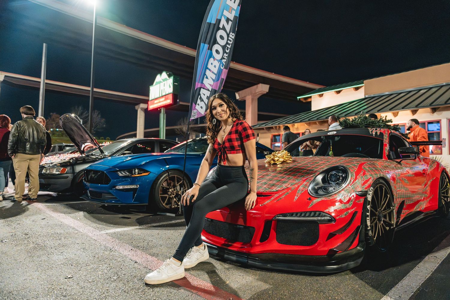 A custom Porsche GT3 RS in red parked next to a blue Ford Mustang at a nighttime car meet.
