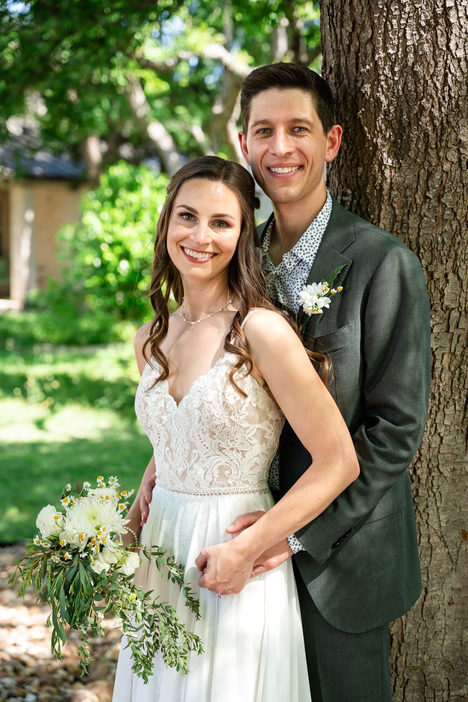 A wedding portrait of a couple posed against a tree trunk in an outdoor garden setting.