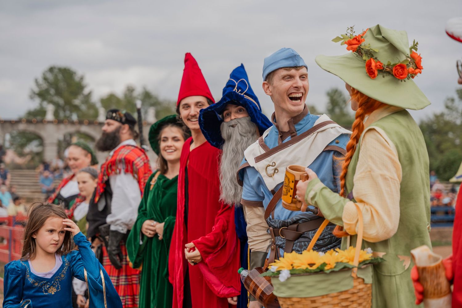 Colorful group of festival performers in medieval costumes with bright hats interacting outdoors.