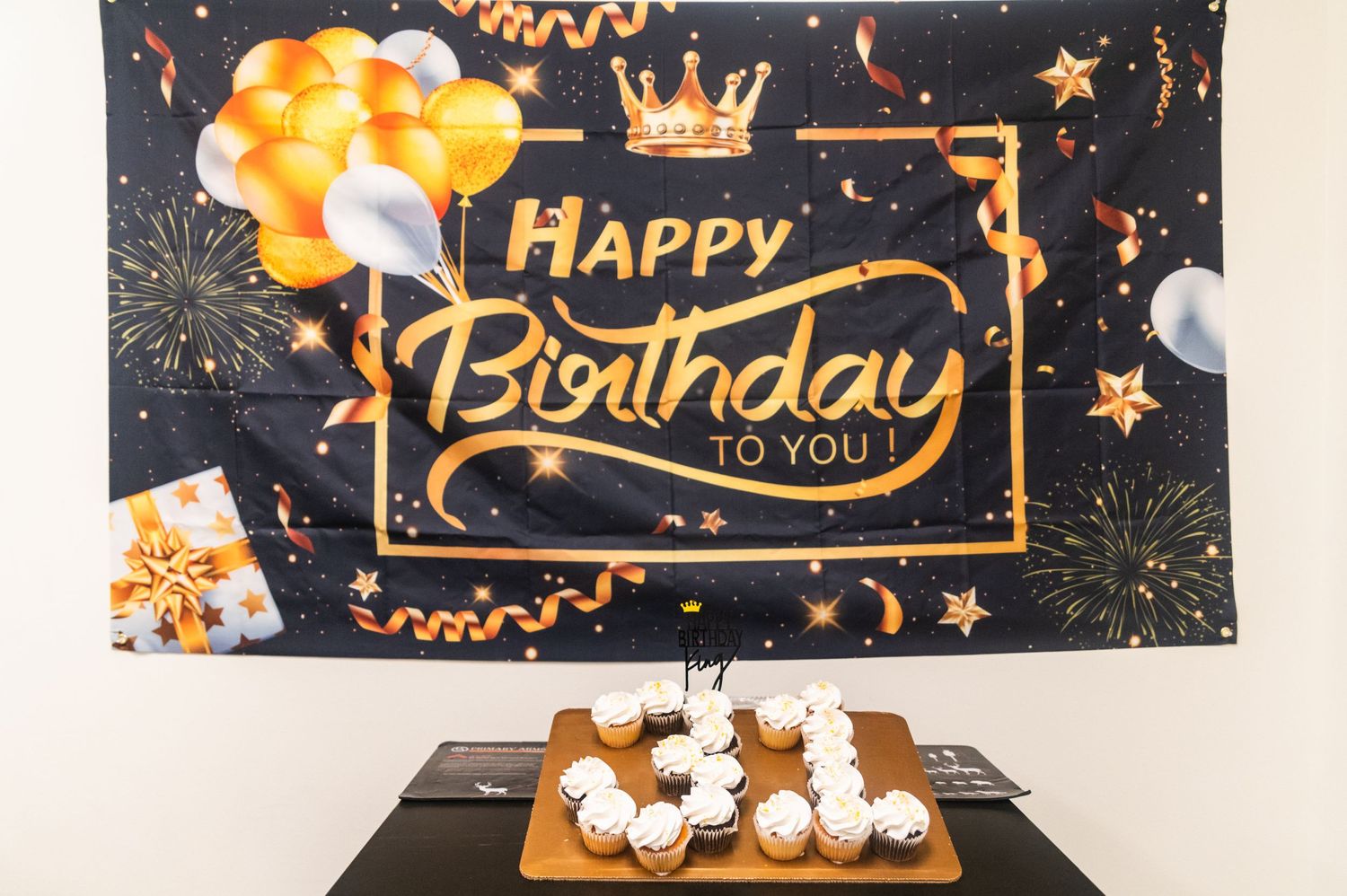Black and gold birthday banner with orange accents displayed above cupcakes.
