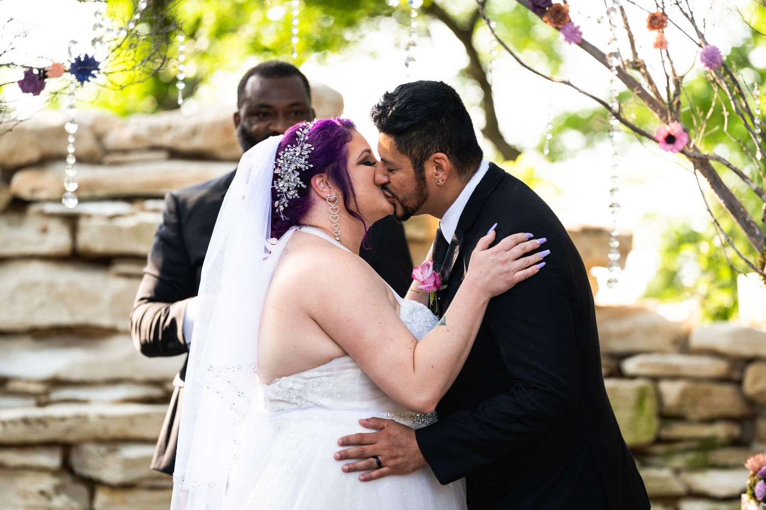 A romantic first kiss moment between newlyweds at an outdoor stone-walled wedding venue.