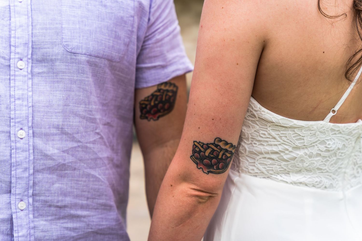 Matching rose tattoos shown on arms of couple in wedding attire.