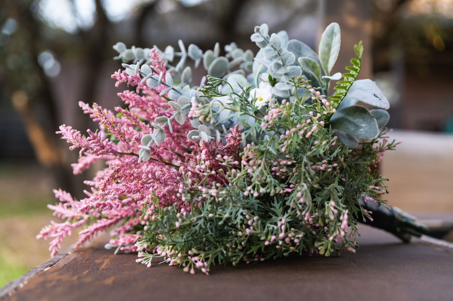 A romantic wedding bouquet with pink and green florals rests on a wooden surface.