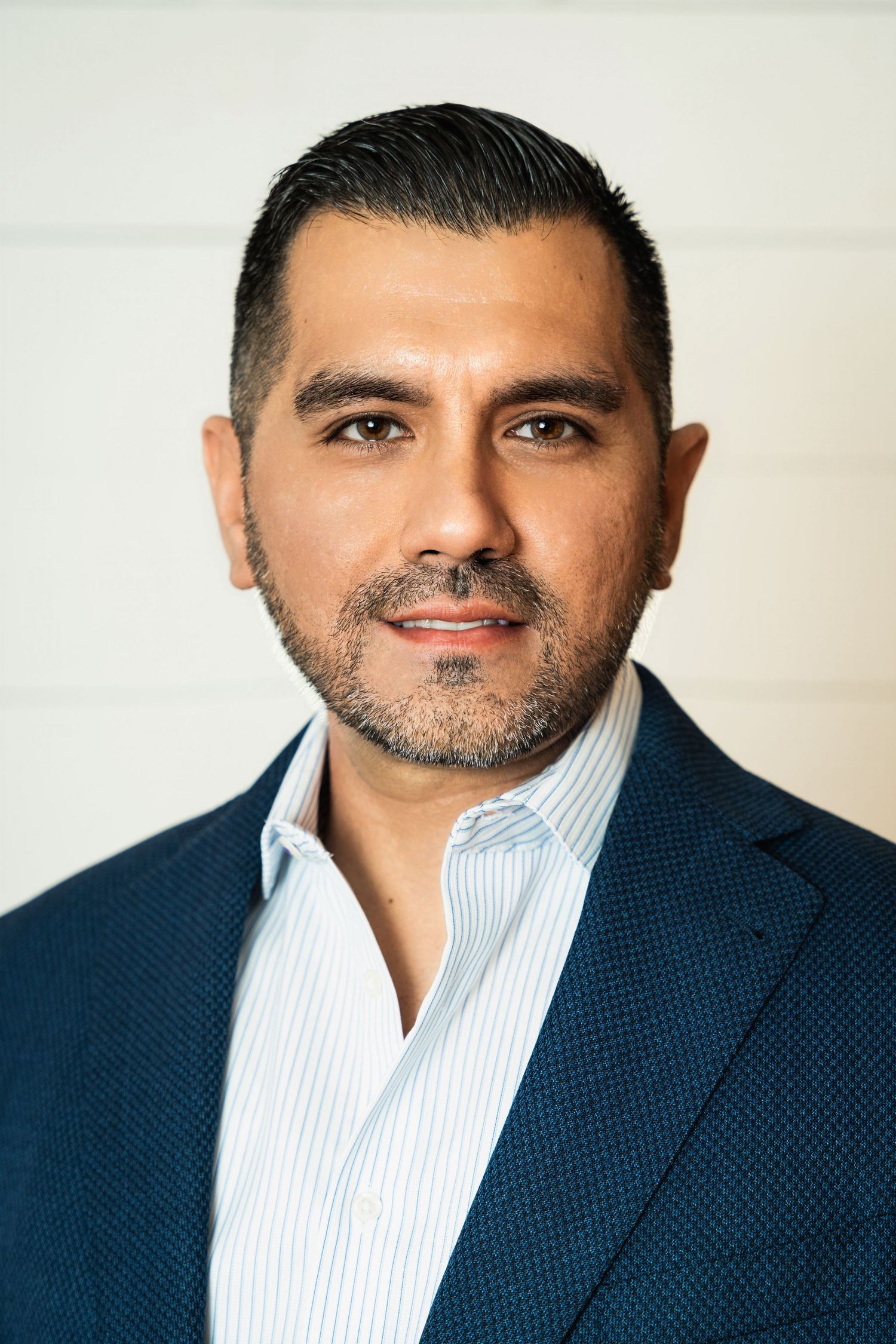 Professional headshot of person in navy blazer and white shirt against light background.