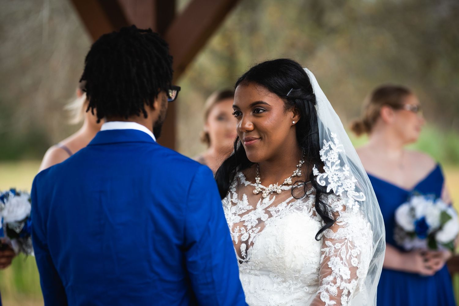 Joyful wedding exchange between bride in detailed lace gown and groom wearing vibrant blue suit.