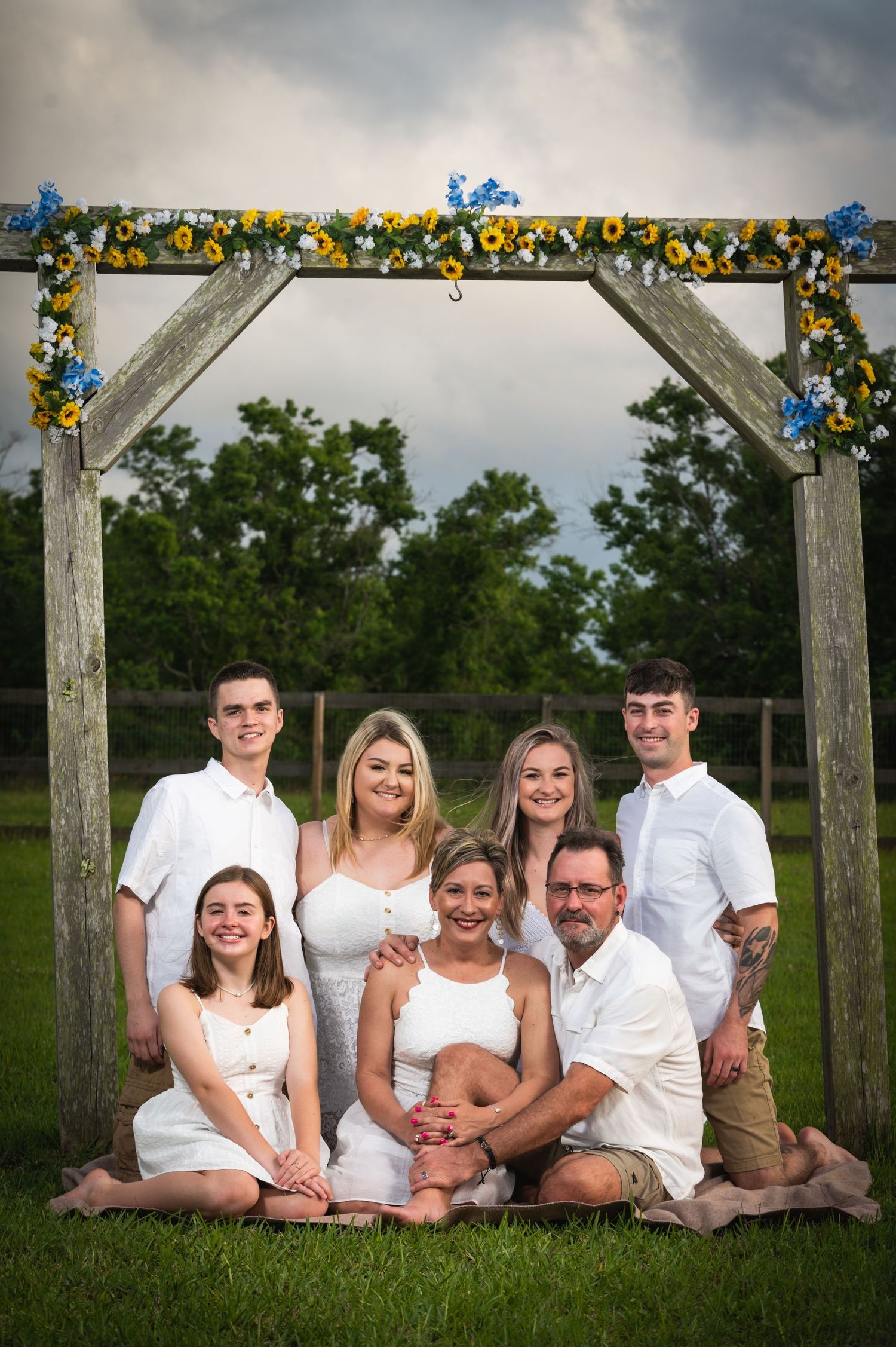 Family portrait under a flower-decorated arch in an outdoor setting.