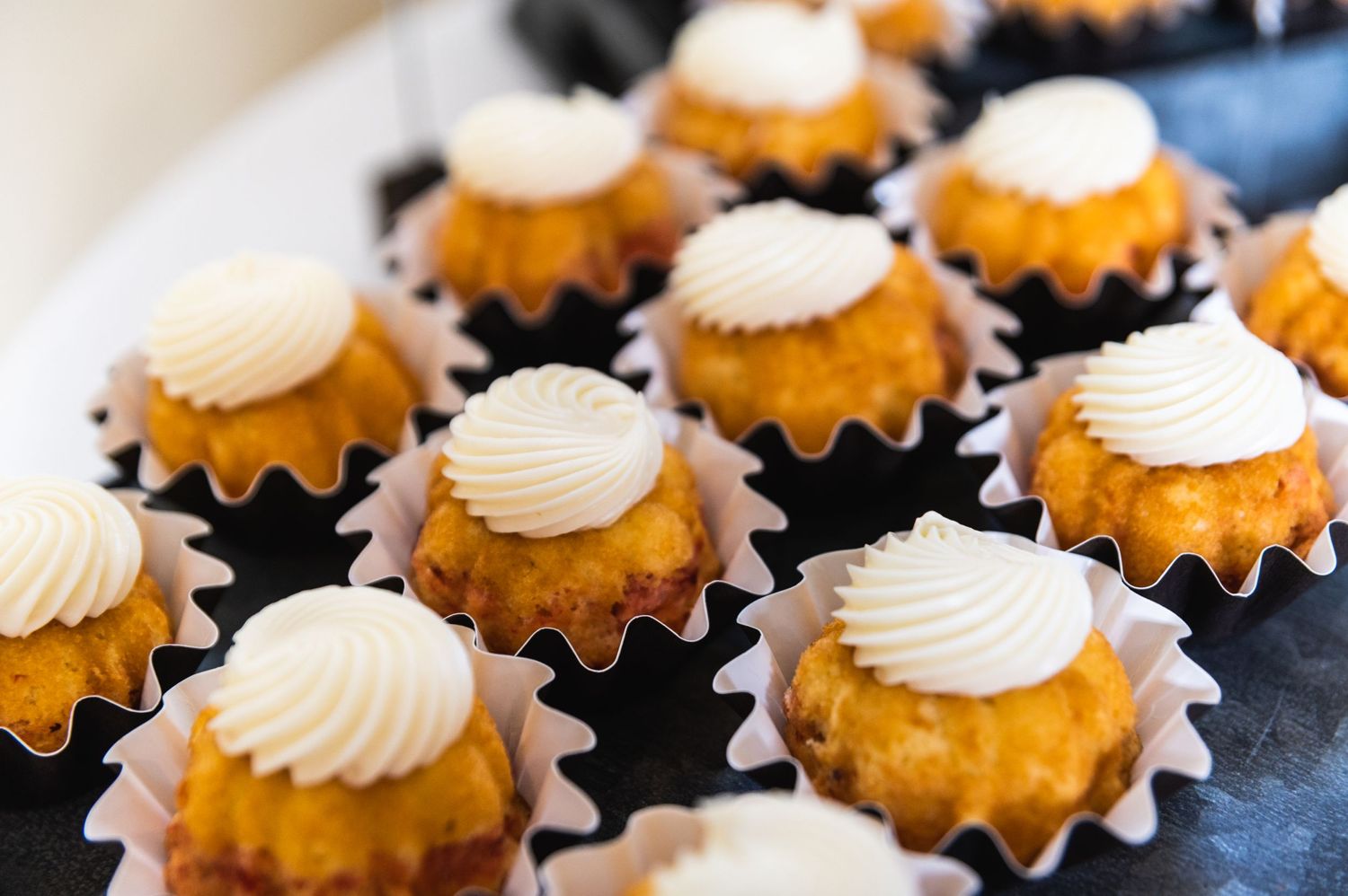 Mini bundt cakes topped with white frosting arranged on black liners.