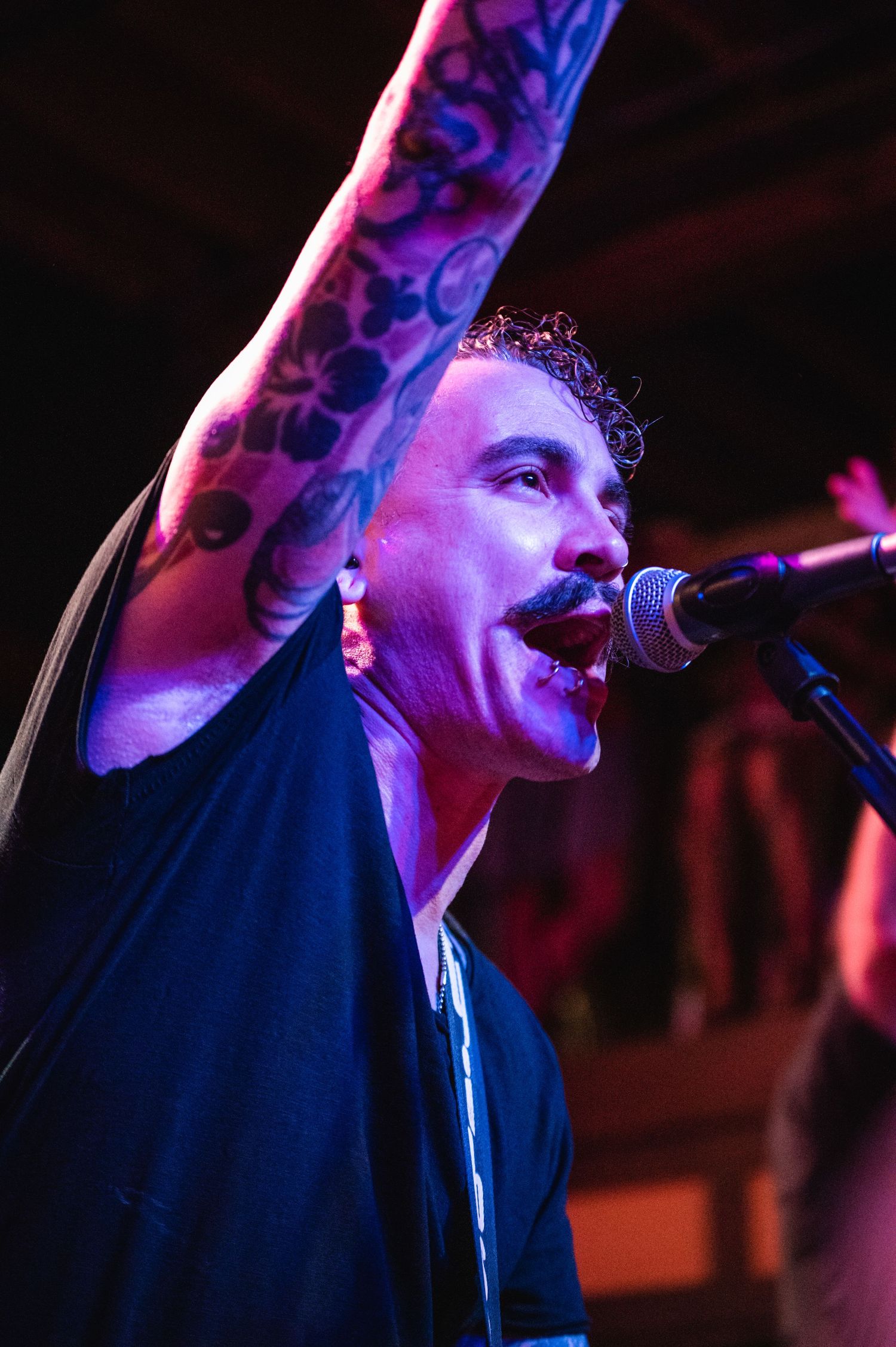 Singer with tattooed arm performing passionately on stage under blue and purple lighting.