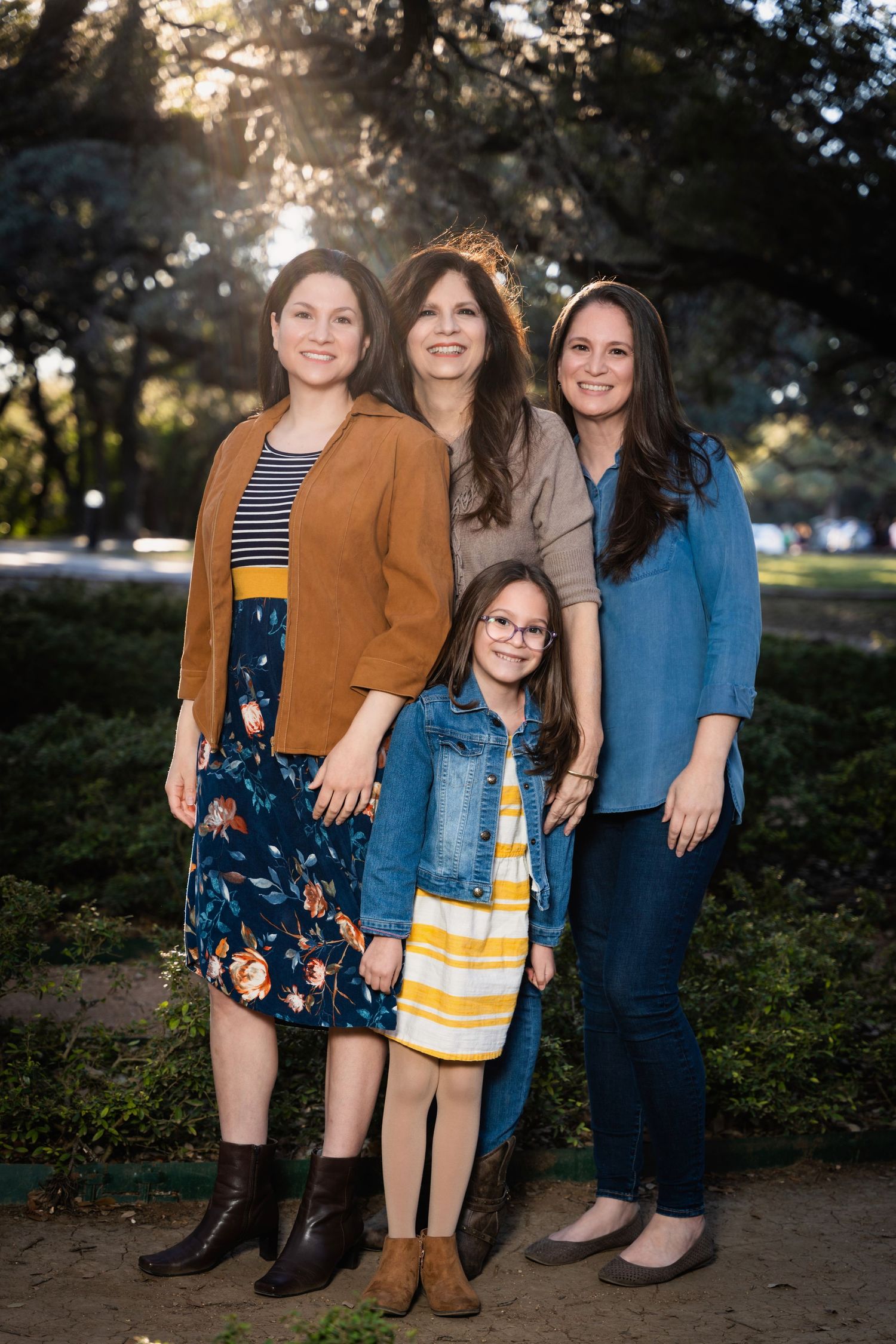 Family portrait of four people in casual attire standing together outdoors at sunset.