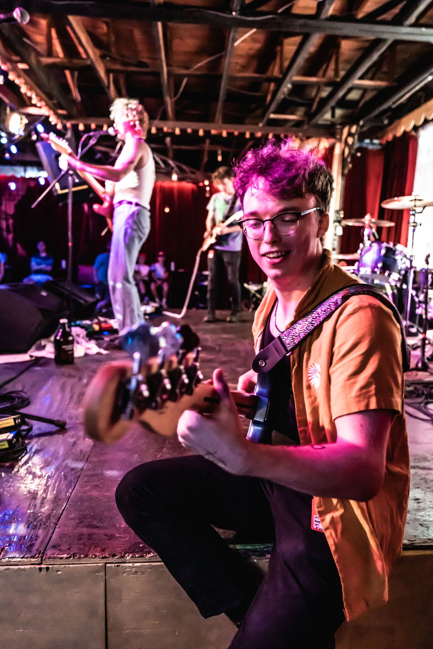 A musician performs on stage with colorful lighting at an indoor concert venue.
