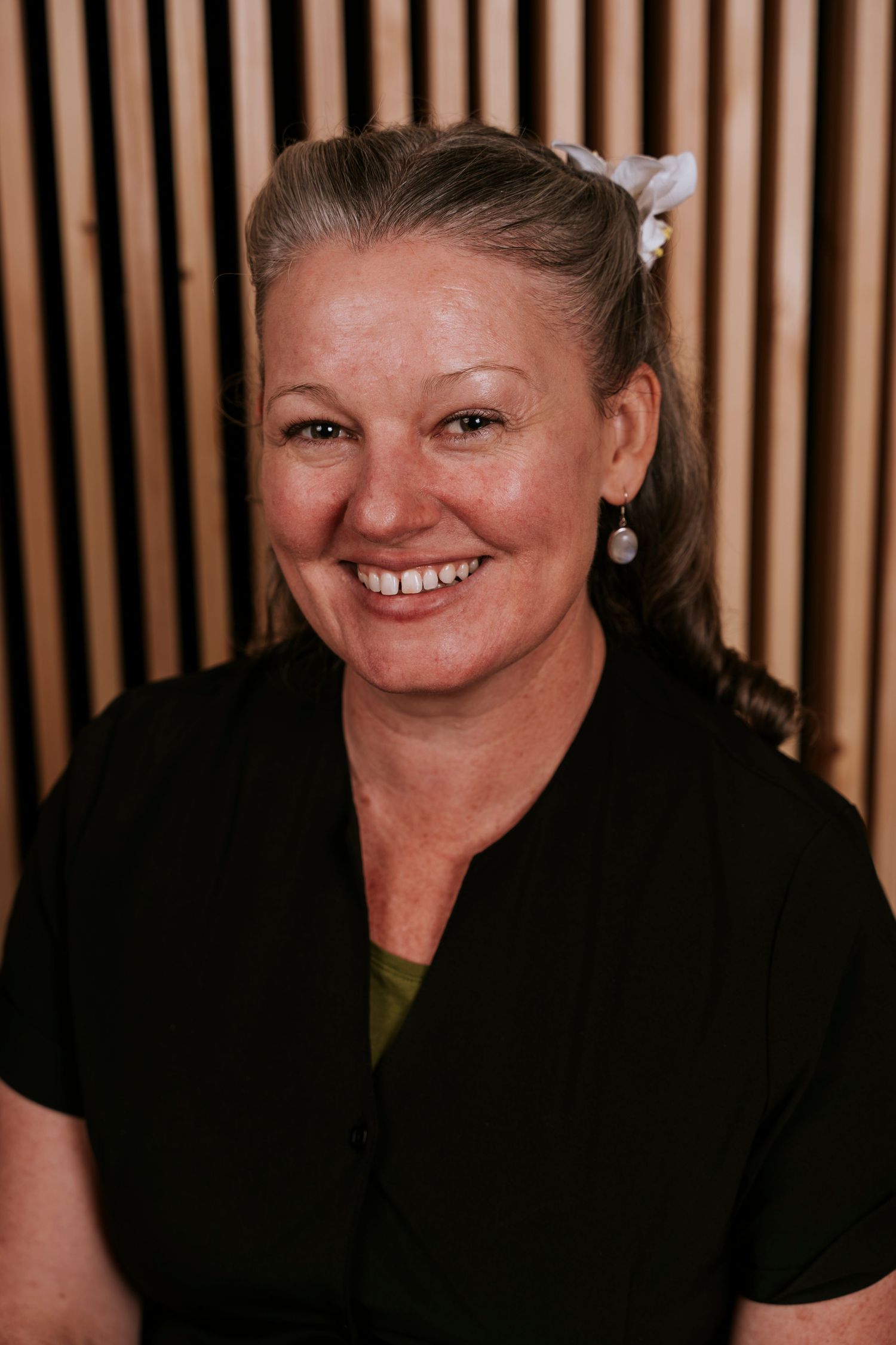 Smiling professional wearing a black top and sparkling earrings poses in front of a slatted wood backdrop.