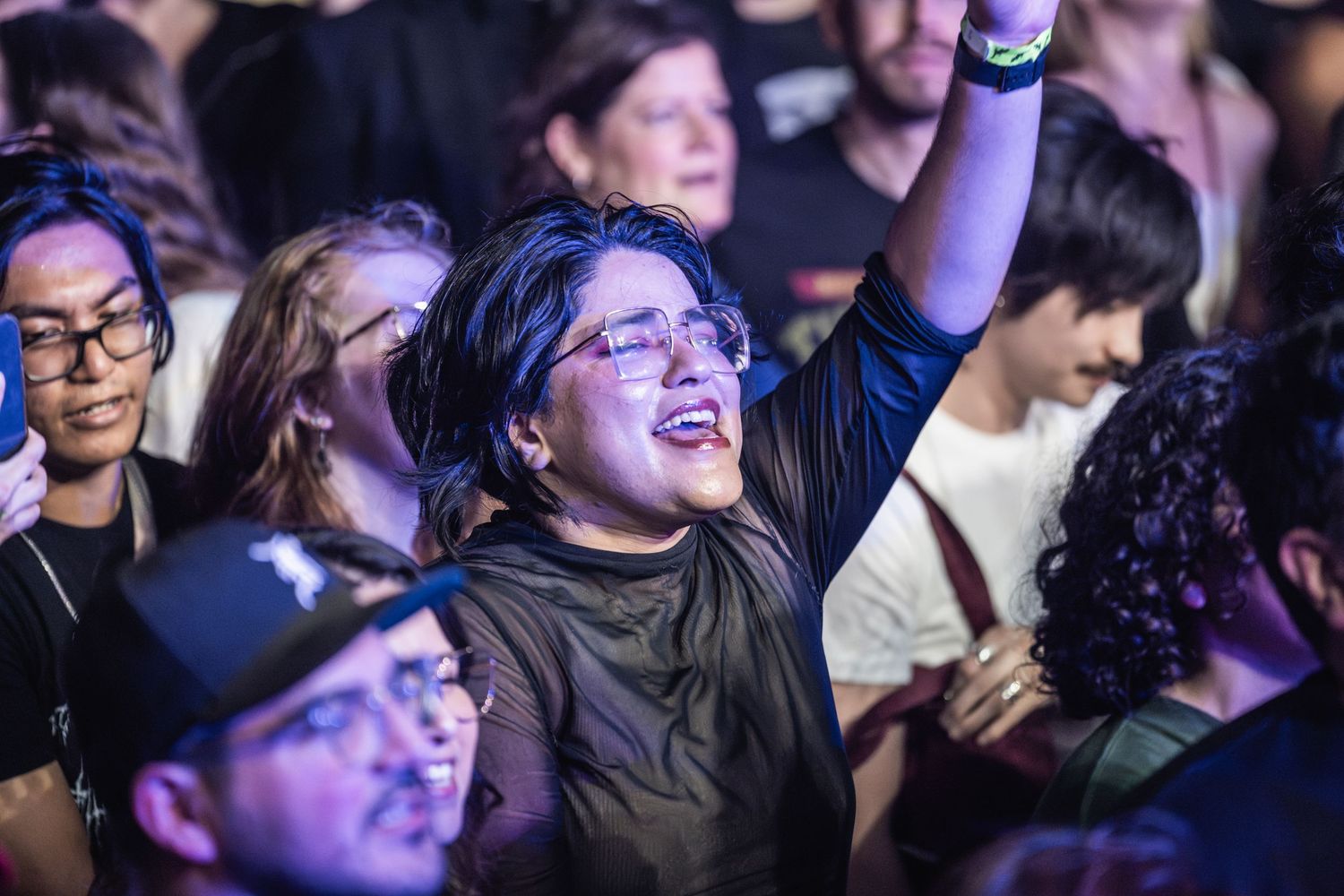 An enthusiastic person in the crowd raises their arm while enjoying a concert among other audience members.