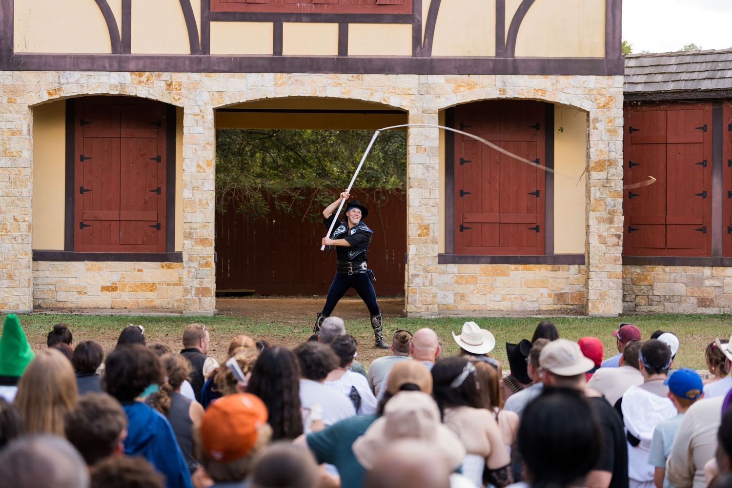 A performer demonstrates sword techniques for a crowd at an outdoor Renaissance faire.