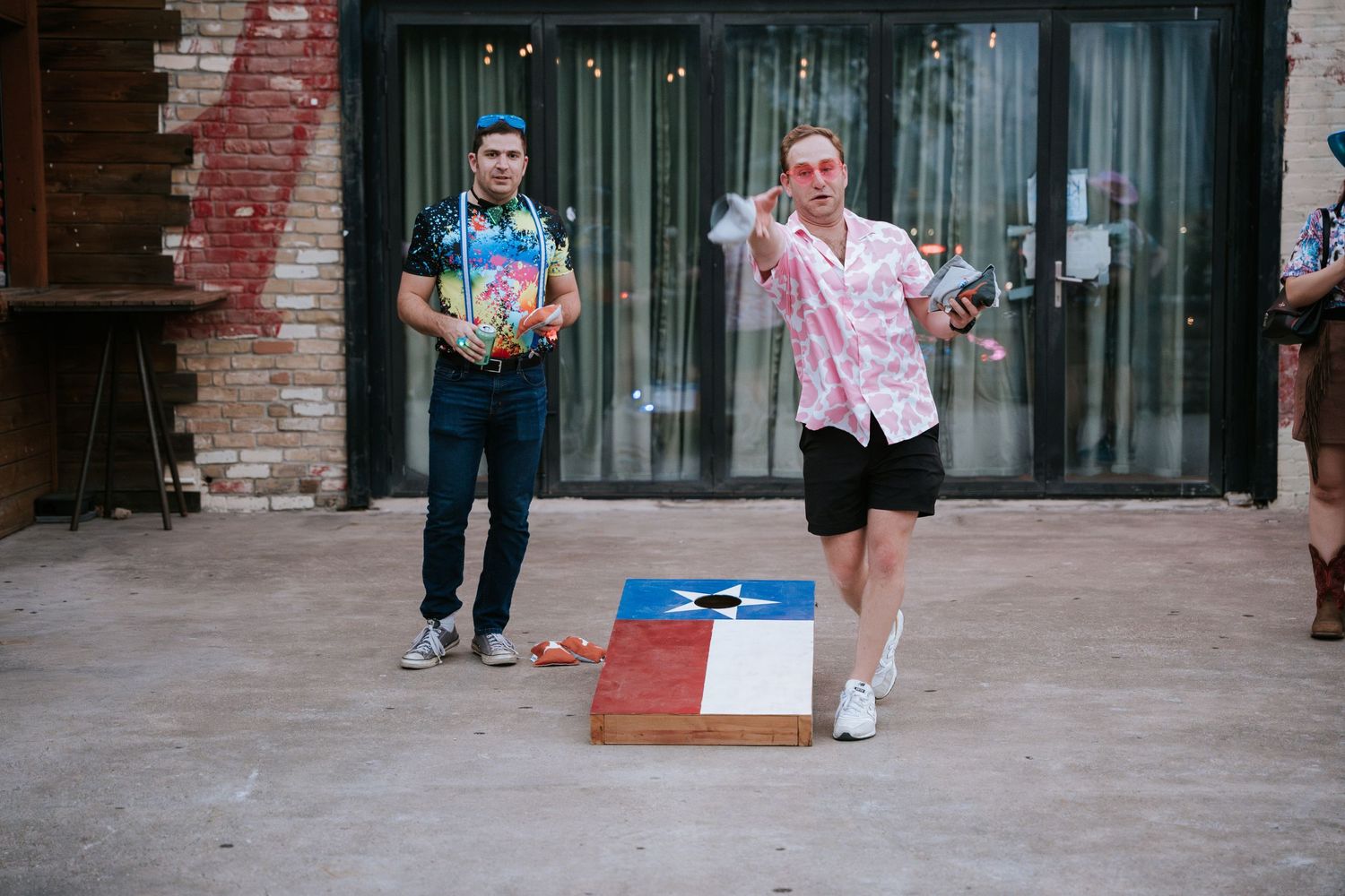 Friends playing cornhole at an outdoor party venue.