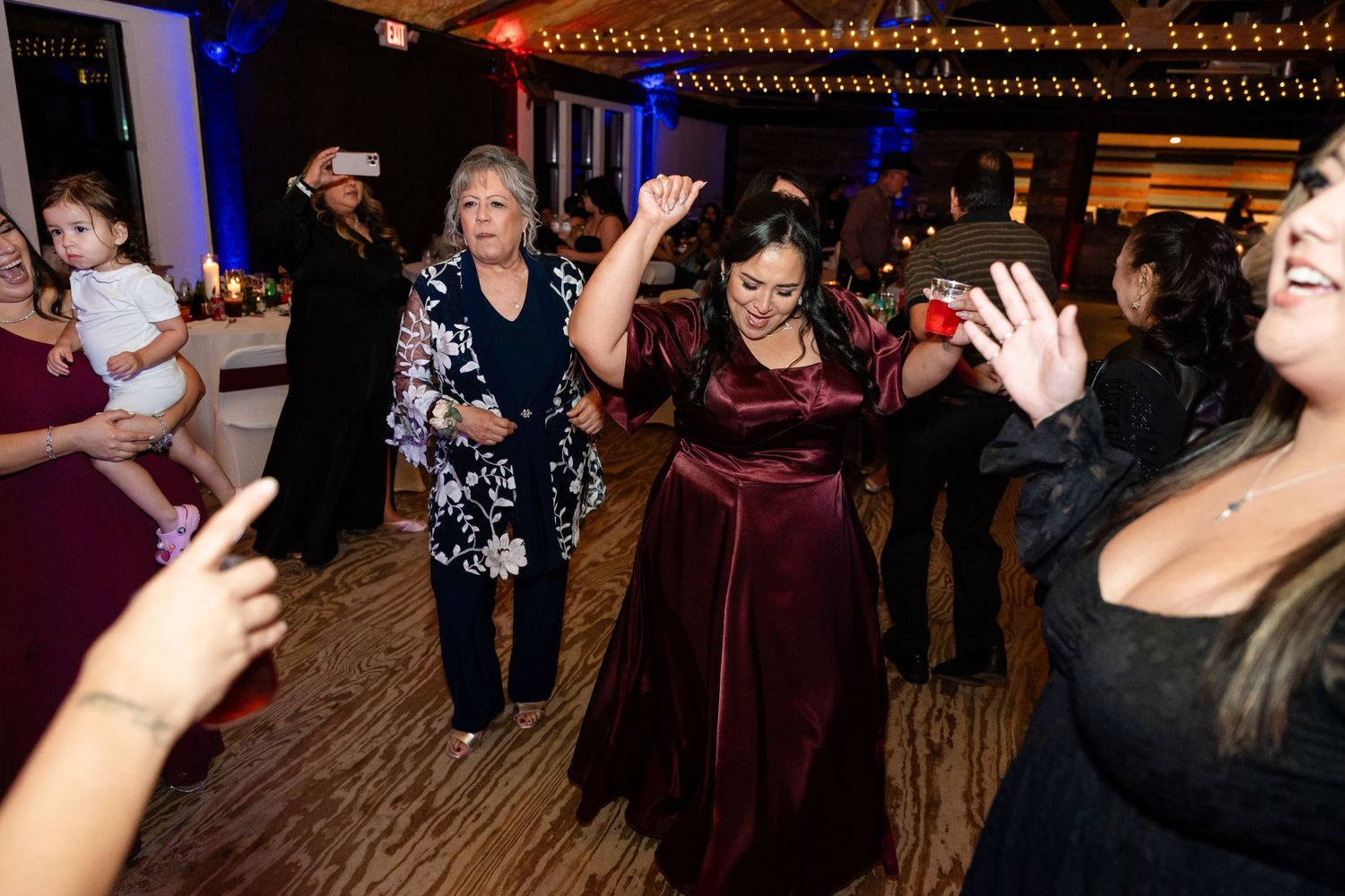 Wedding guests dancing and celebrating with raised hands under blue mood lighting.