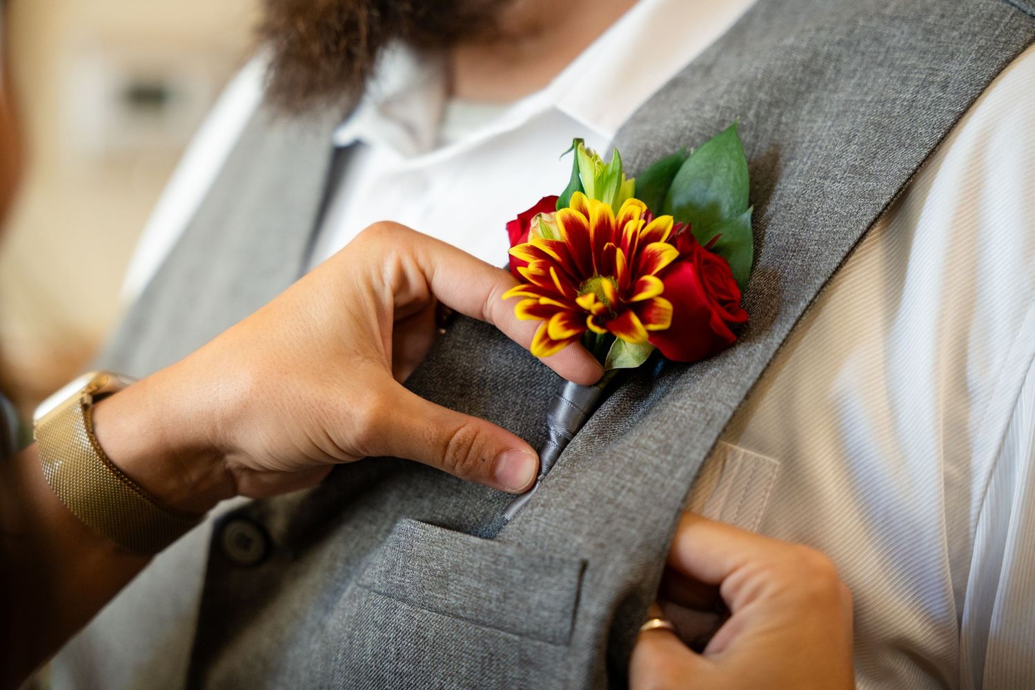 Red and yellow dahlia boutonniere being pinned on grey suit vest.