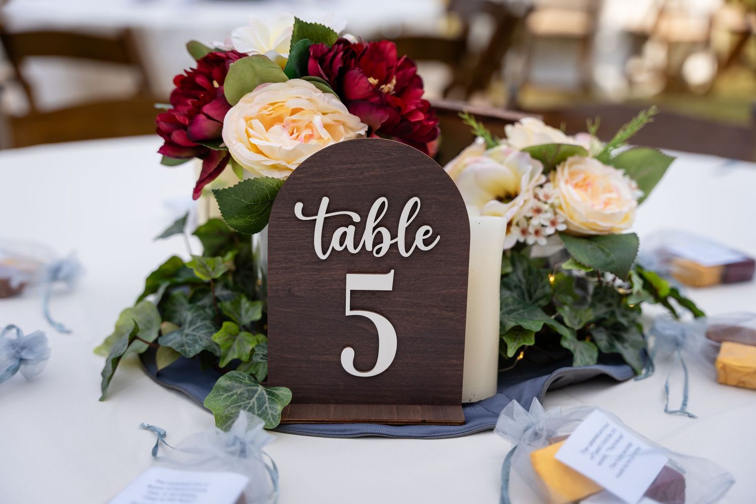Close-up of rustic wooden table number 5 sign with burgundy and cream floral arrangement.