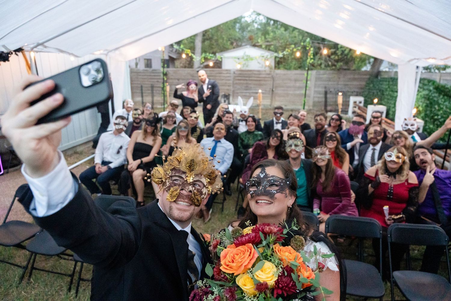 Wedding guests wearing masks take a celebratory selfie with colorful flowers.