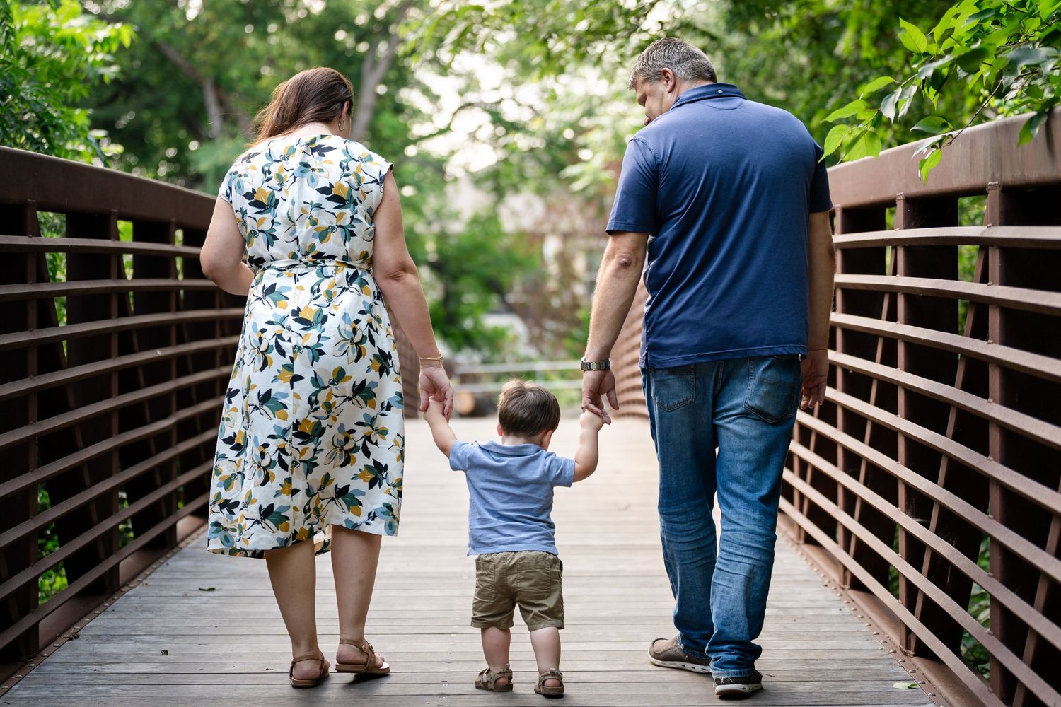 A family walking away hand-in-hand on a wooden bridge surrounded by greenery.