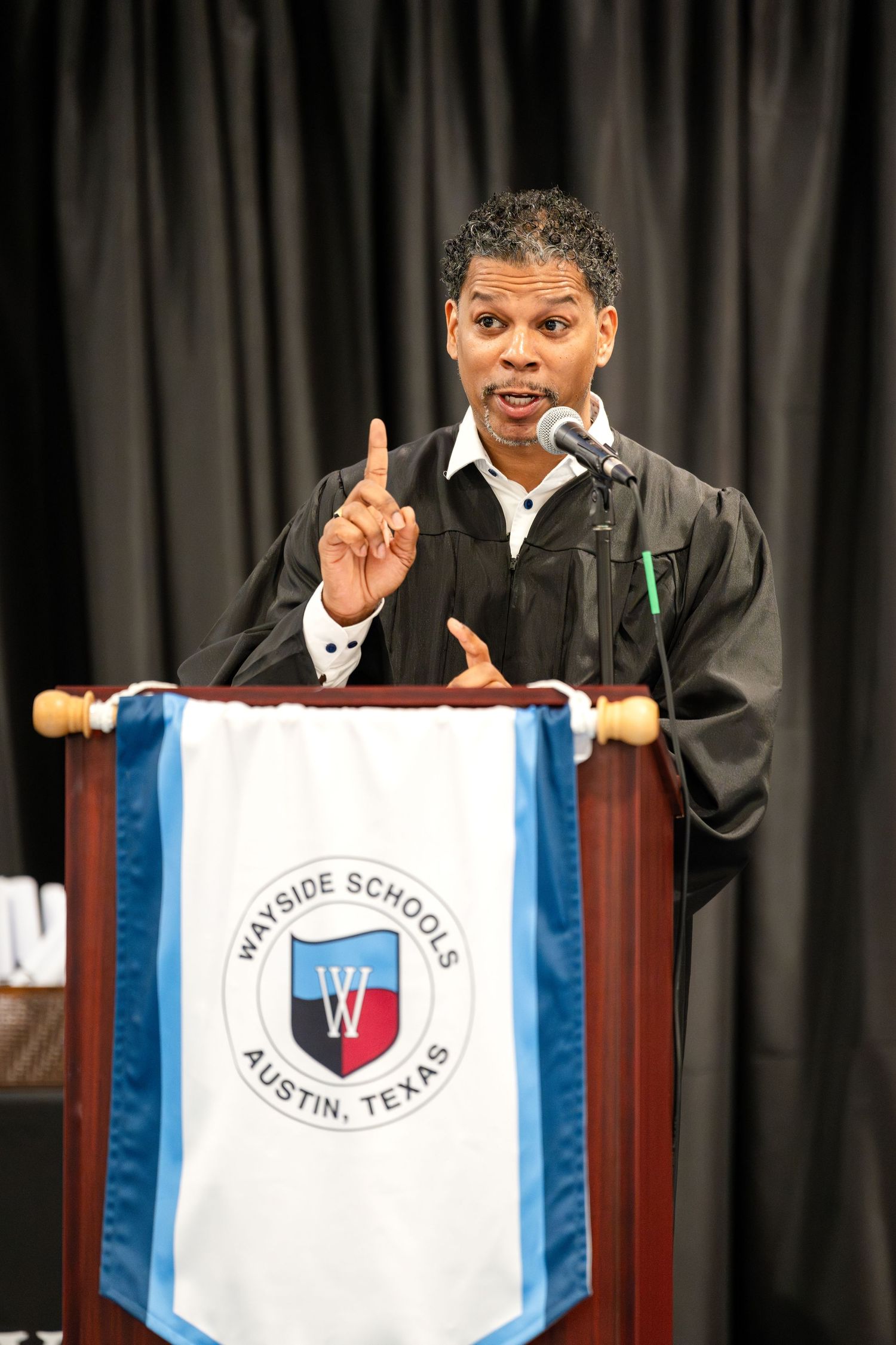 Speaker in academic regalia addresses audience at Westside Schools in Austin, Texas.