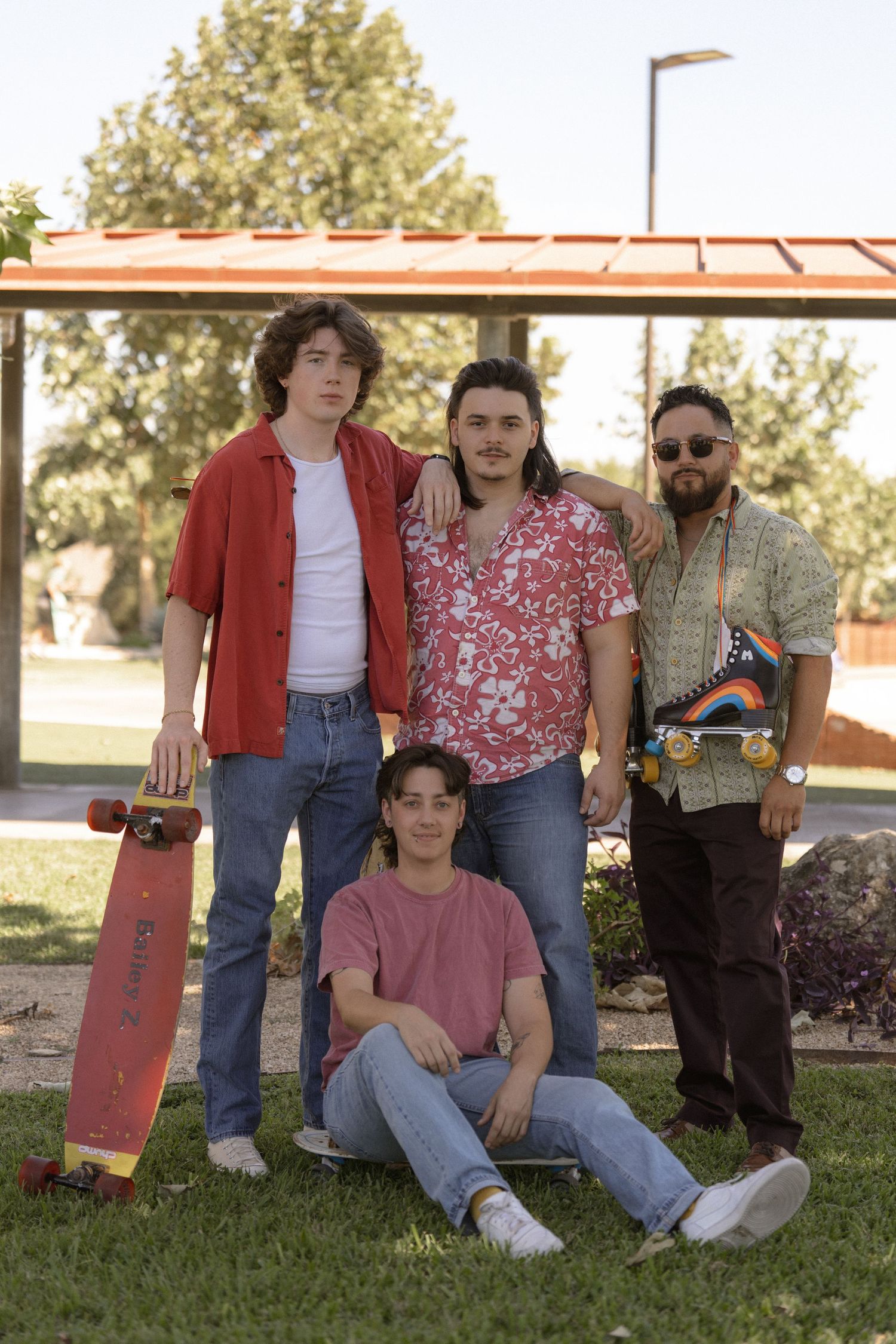 Group of friends posing with skateboard outdoors on grass near building.