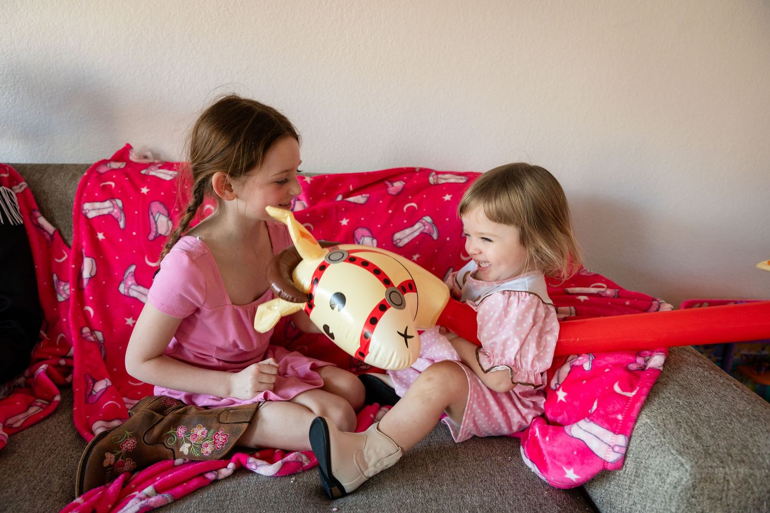 Two people sit on a red patterned couch playing with a stuffed animal toy together.