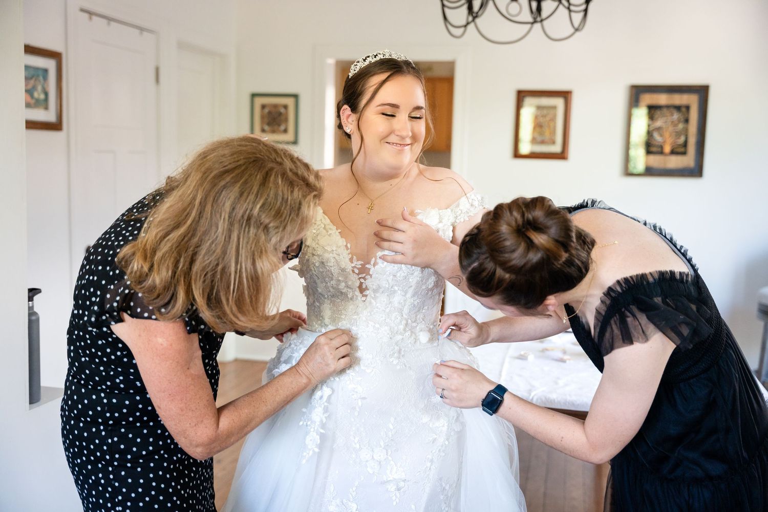 A group helps adjust a wedding dress during final preparations indoors.