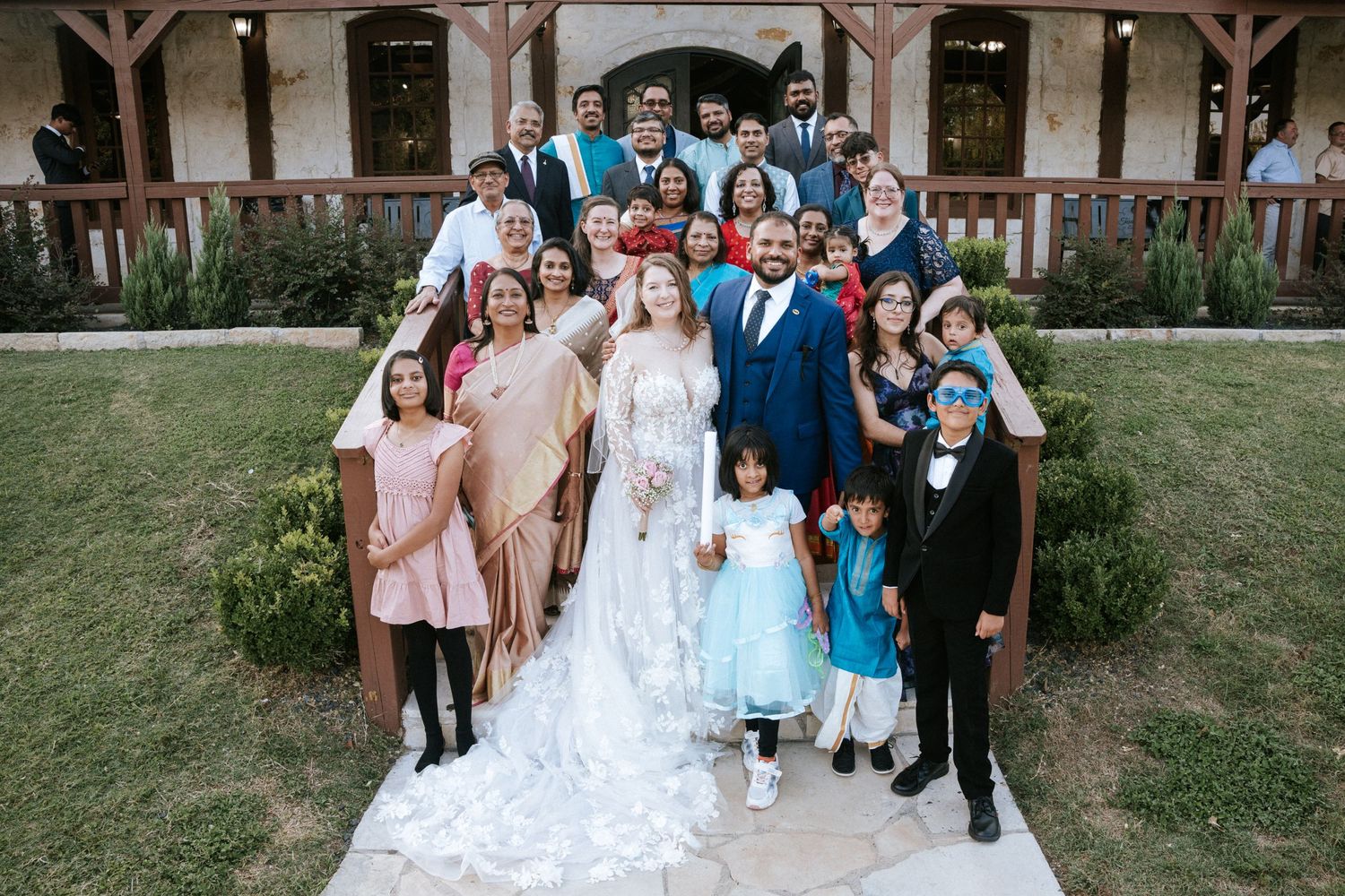 Large wedding party group photo with bridesmaids in blue and the bride in white lace.