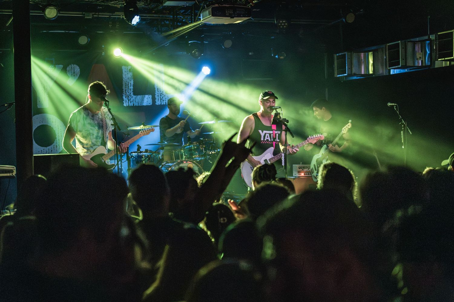 Performers on stage at a concert venue with dramatic green and blue lighting effects.