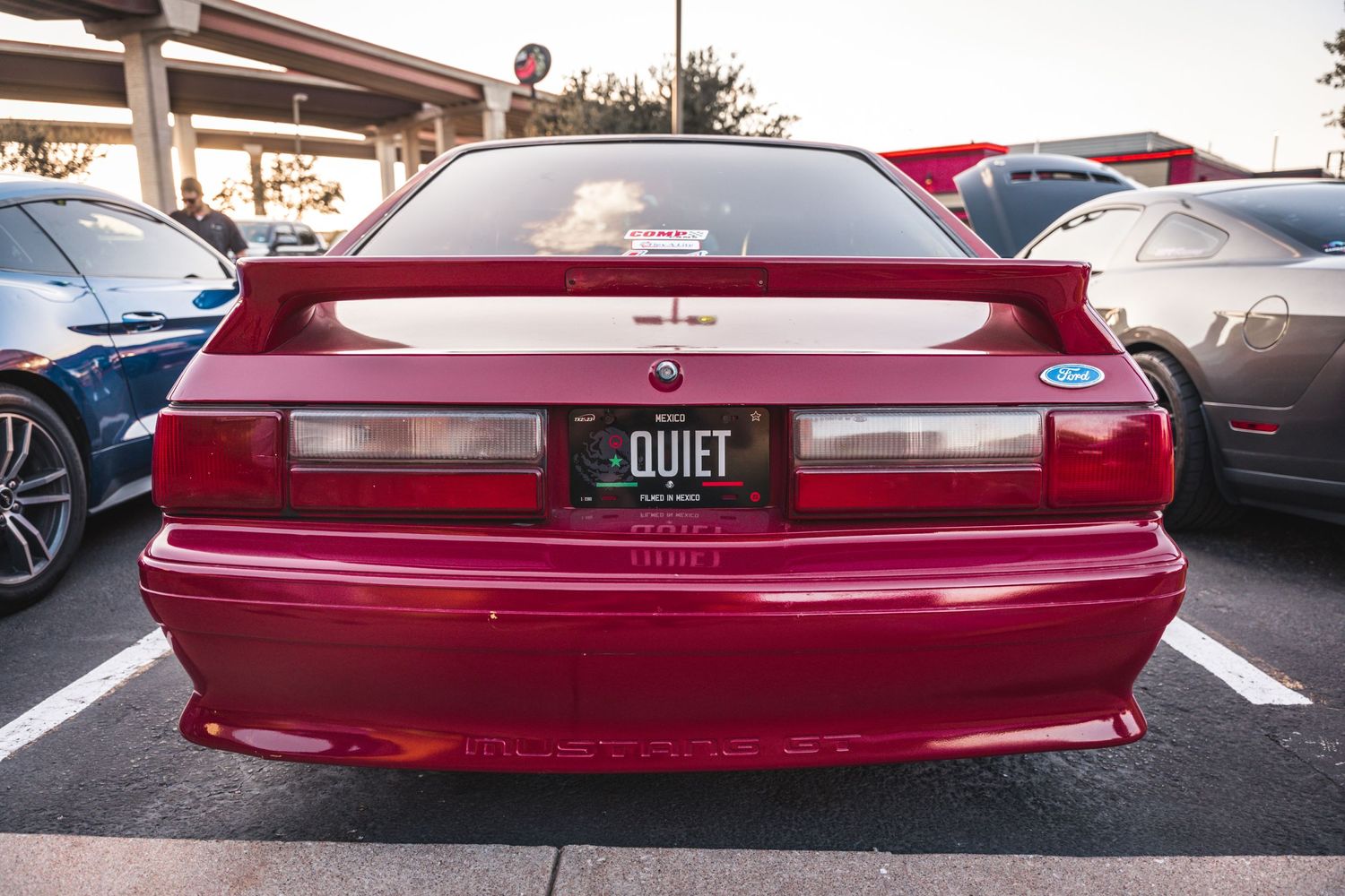 Rear view of a red vintage car with custom license plate in a parking lot.