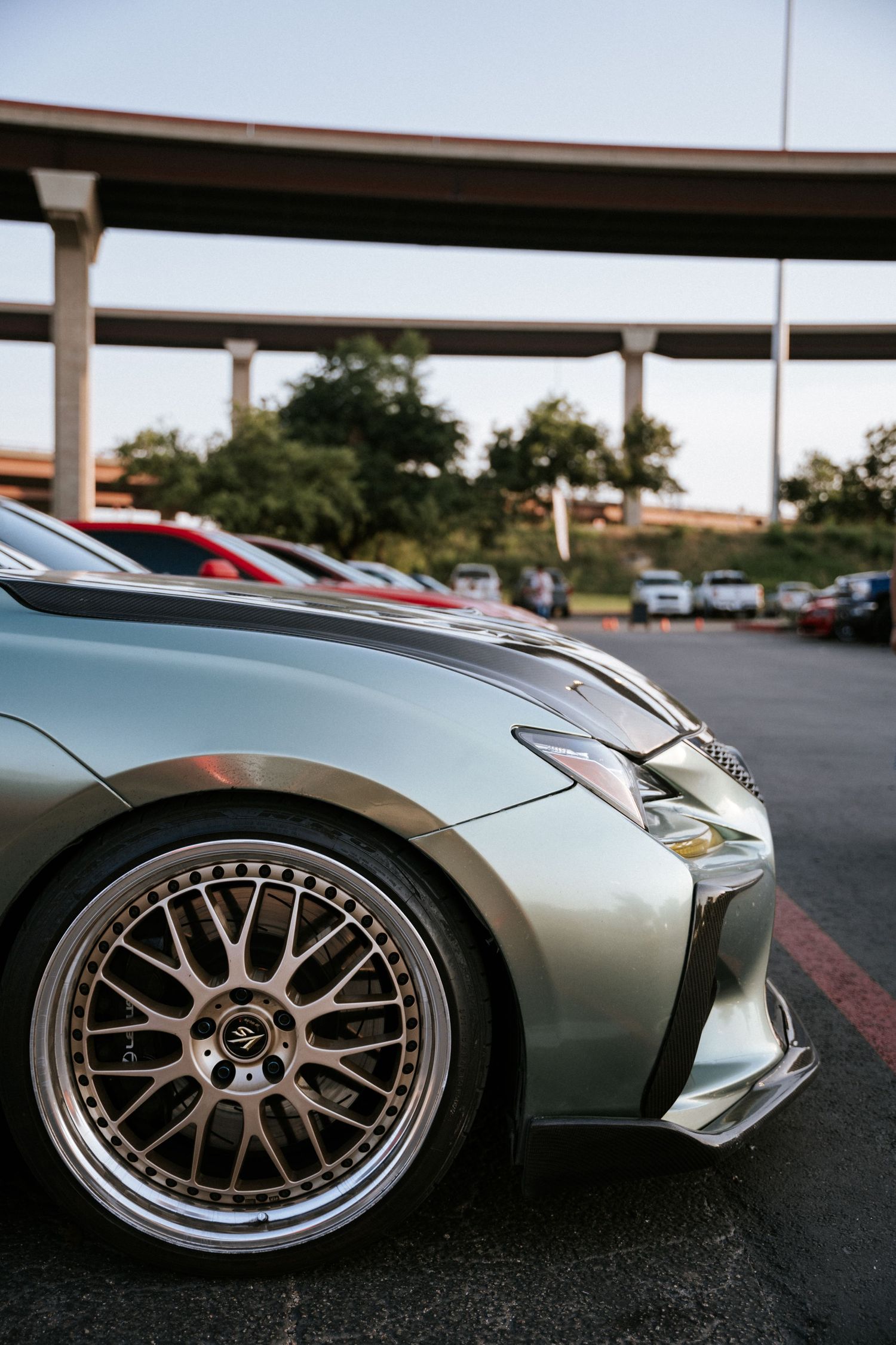 Modified sports car with custom BBS wheels and aggressive body kit under highway overpass.