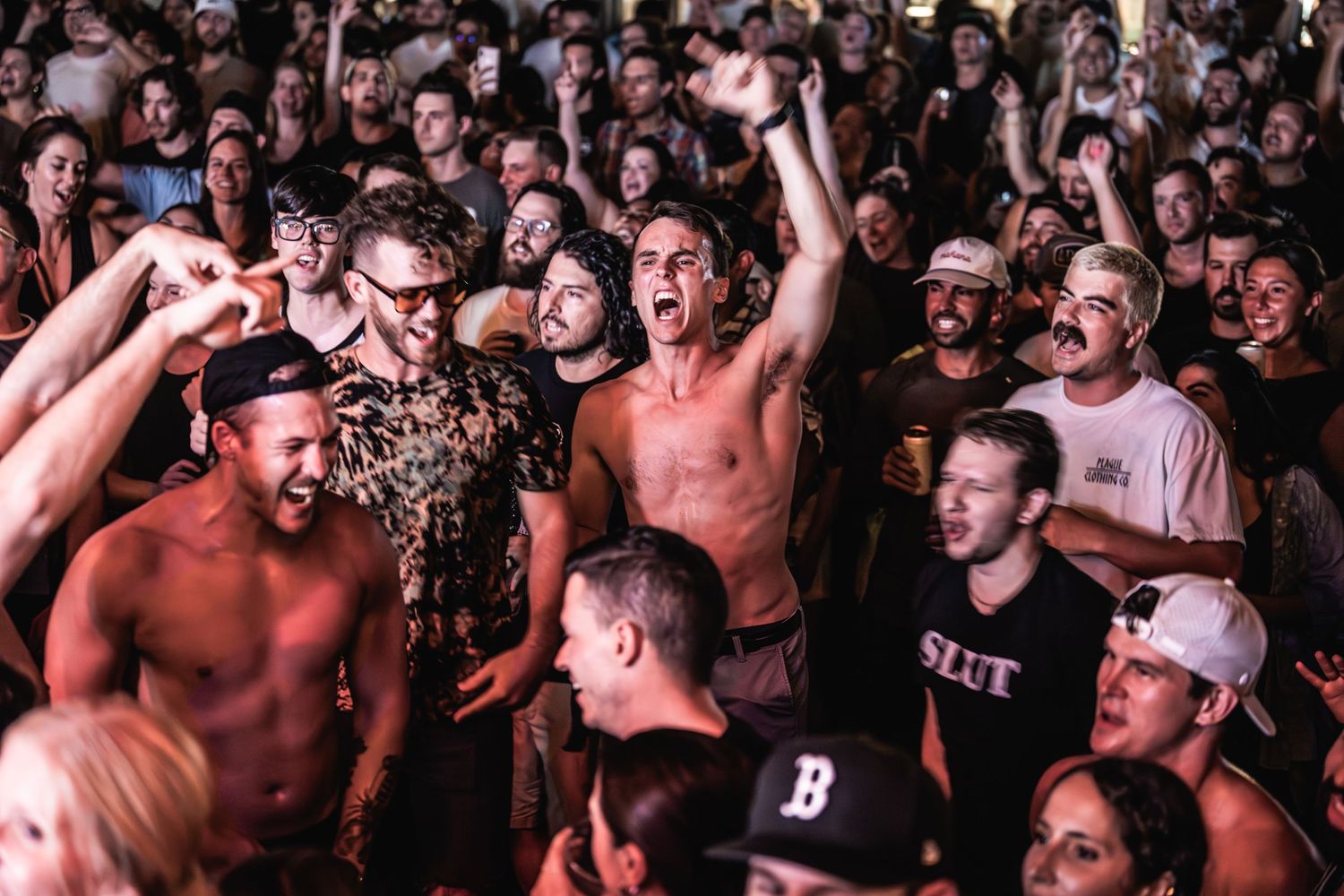 Energetic concert crowd cheering and moshing during a live performance.