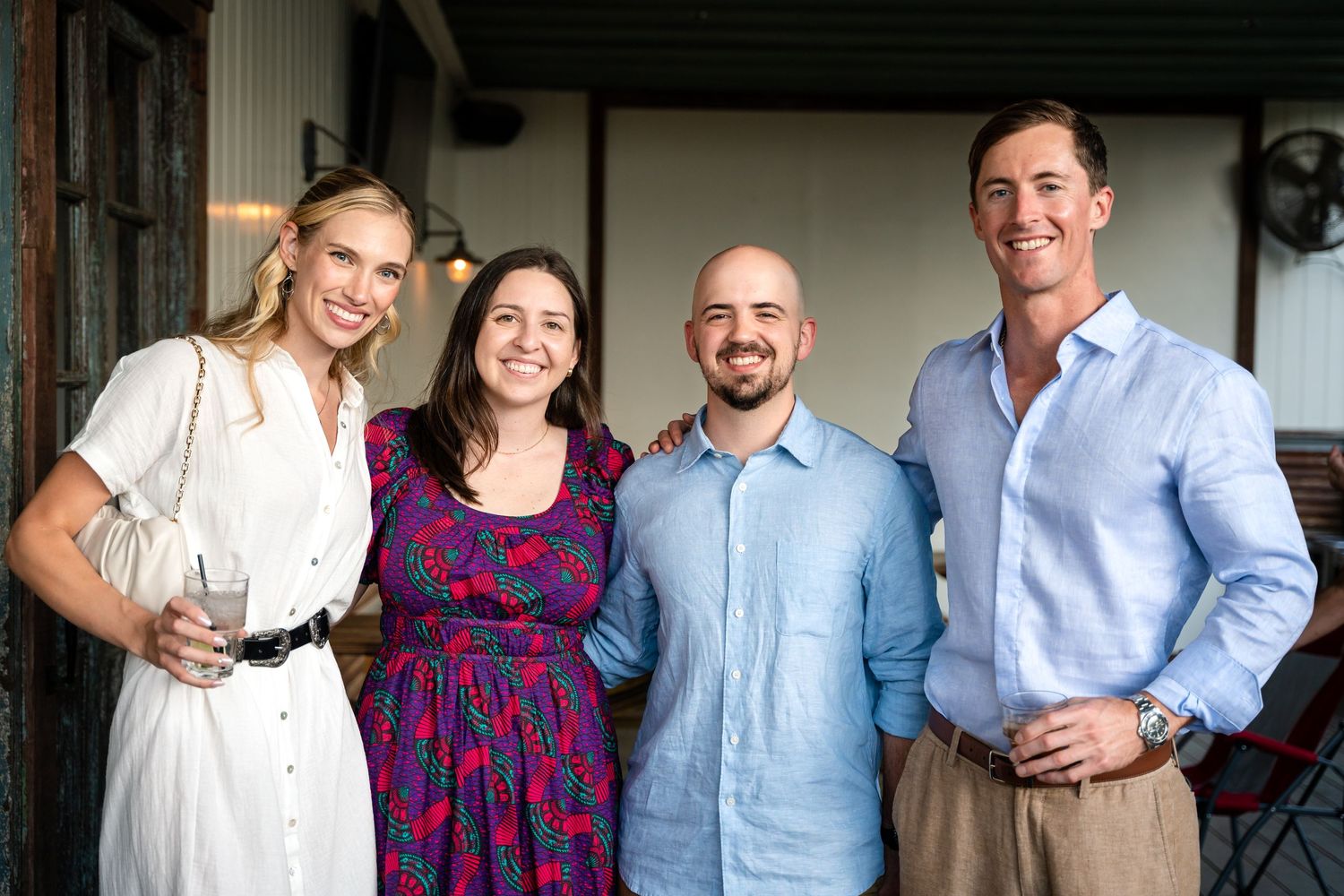 Group of friends smile together at an outdoor gathering wearing casual summer attire.