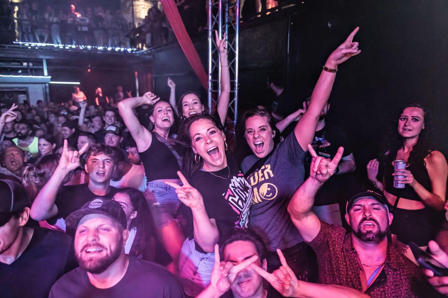 Concert crowd cheering enthusiastically at a rock show with colorful purple lighting.