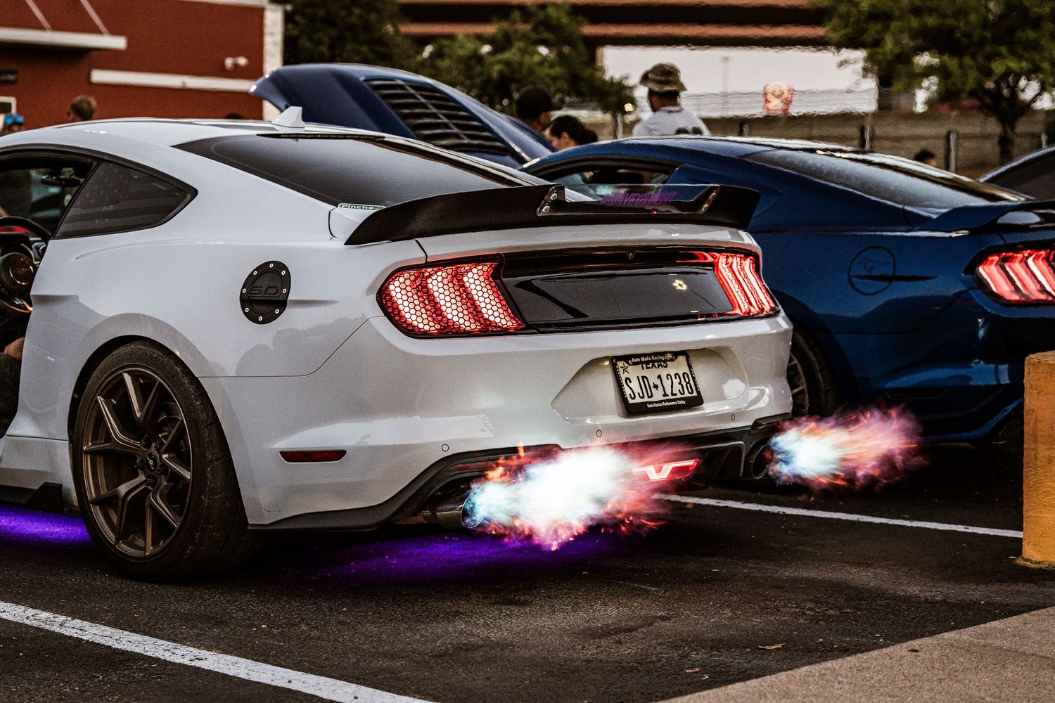 Modified Ford Mustang with aftermarket exhaust shooting purple flames in dark parking lot.